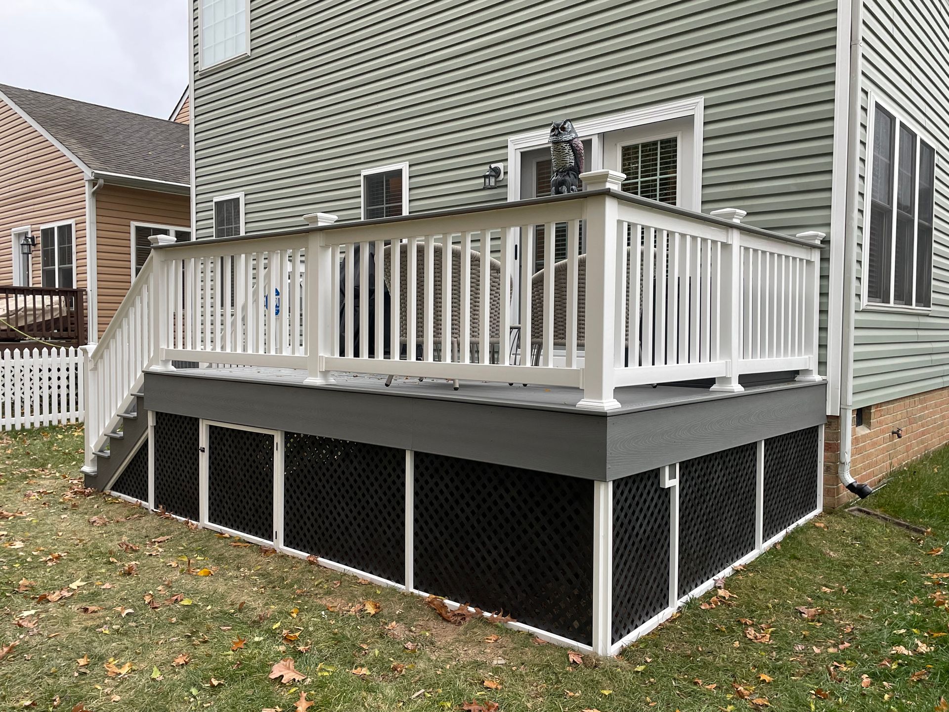 Small gray house deck with white railings and enclosed black lattice skirting beside a yard.