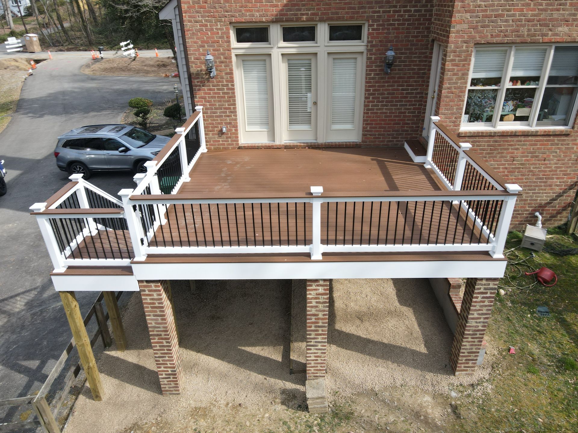 Brick house deck with white railing and steps, viewed from above, beside a parked black car.