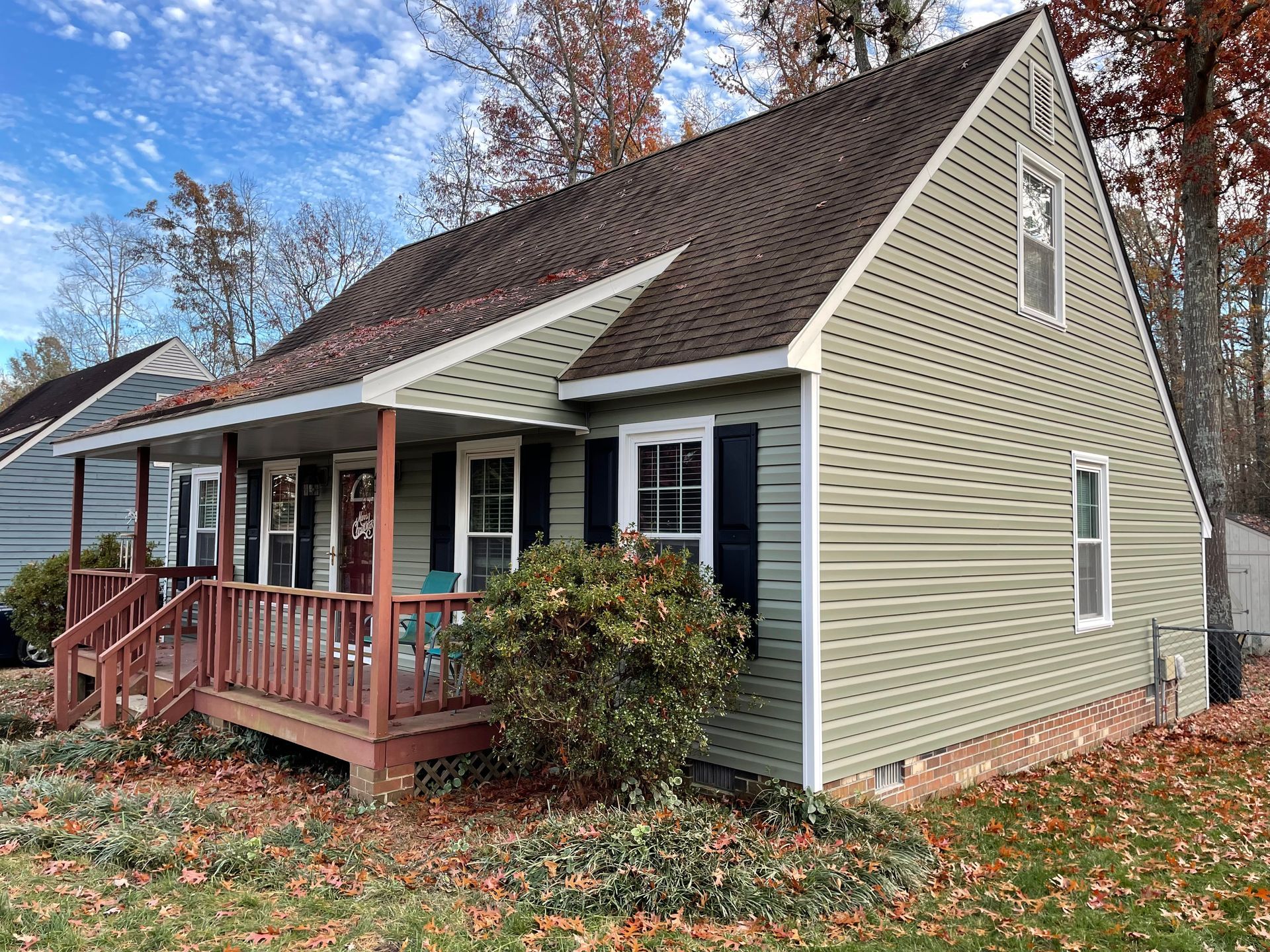 Small beige house with a brown roof, red porch, and autumn leaves in the yard