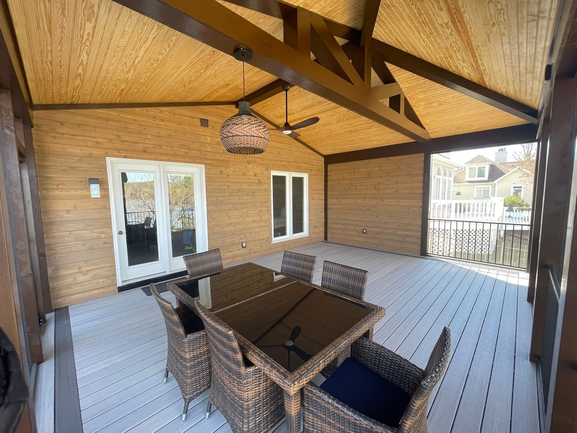 Covered patio with wicker dining set, white floor, and wood-paneled ceiling with fan and skylight.