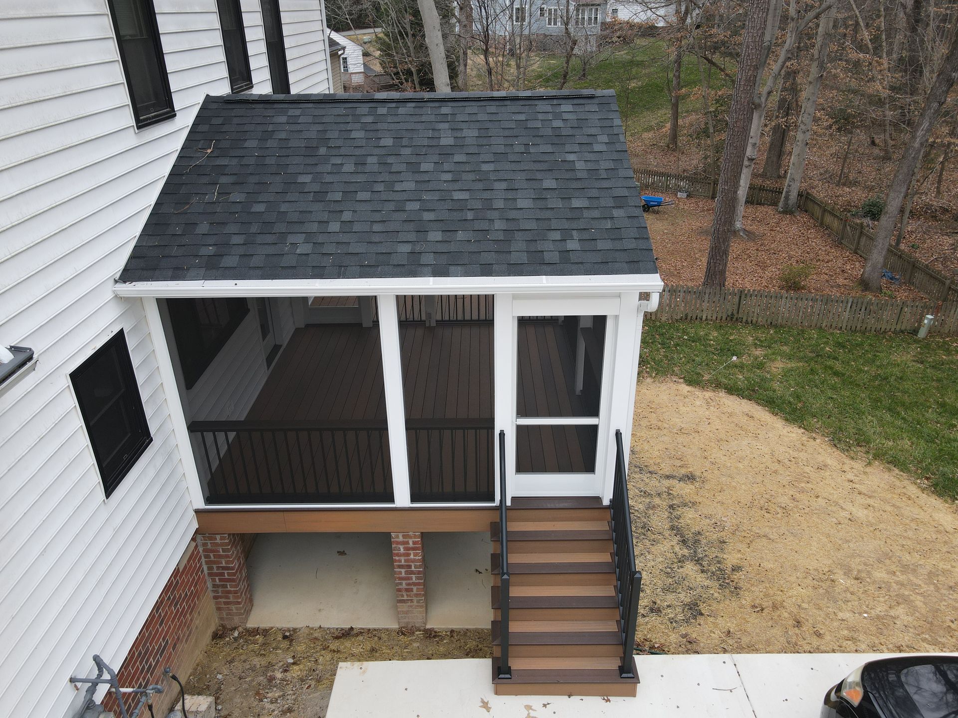 Small covered porch with stairs, white railings, and a black roof beside a house.