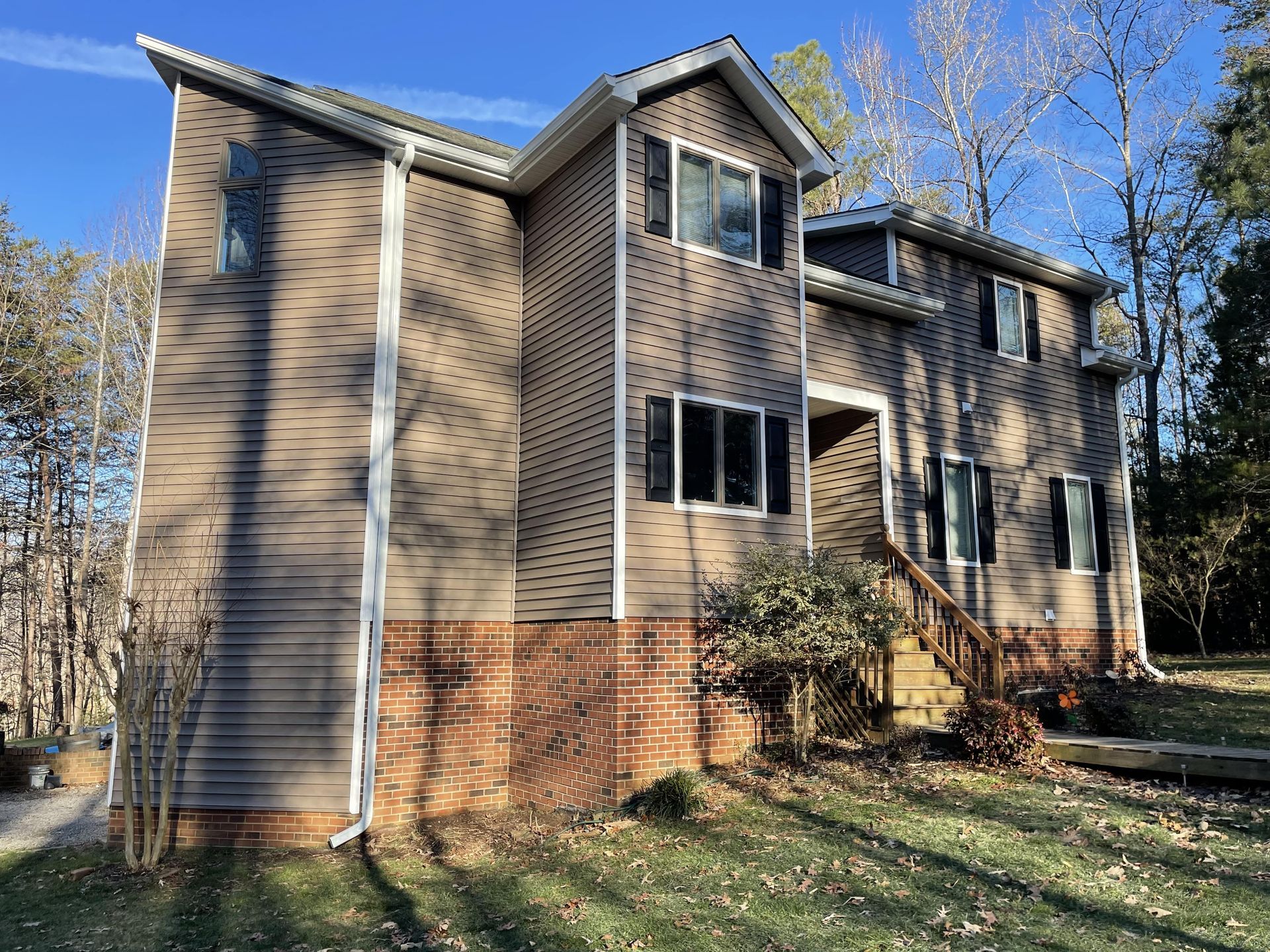 Two-story beige house with brick lower exterior and white-trimmed windows in a wooded yard
