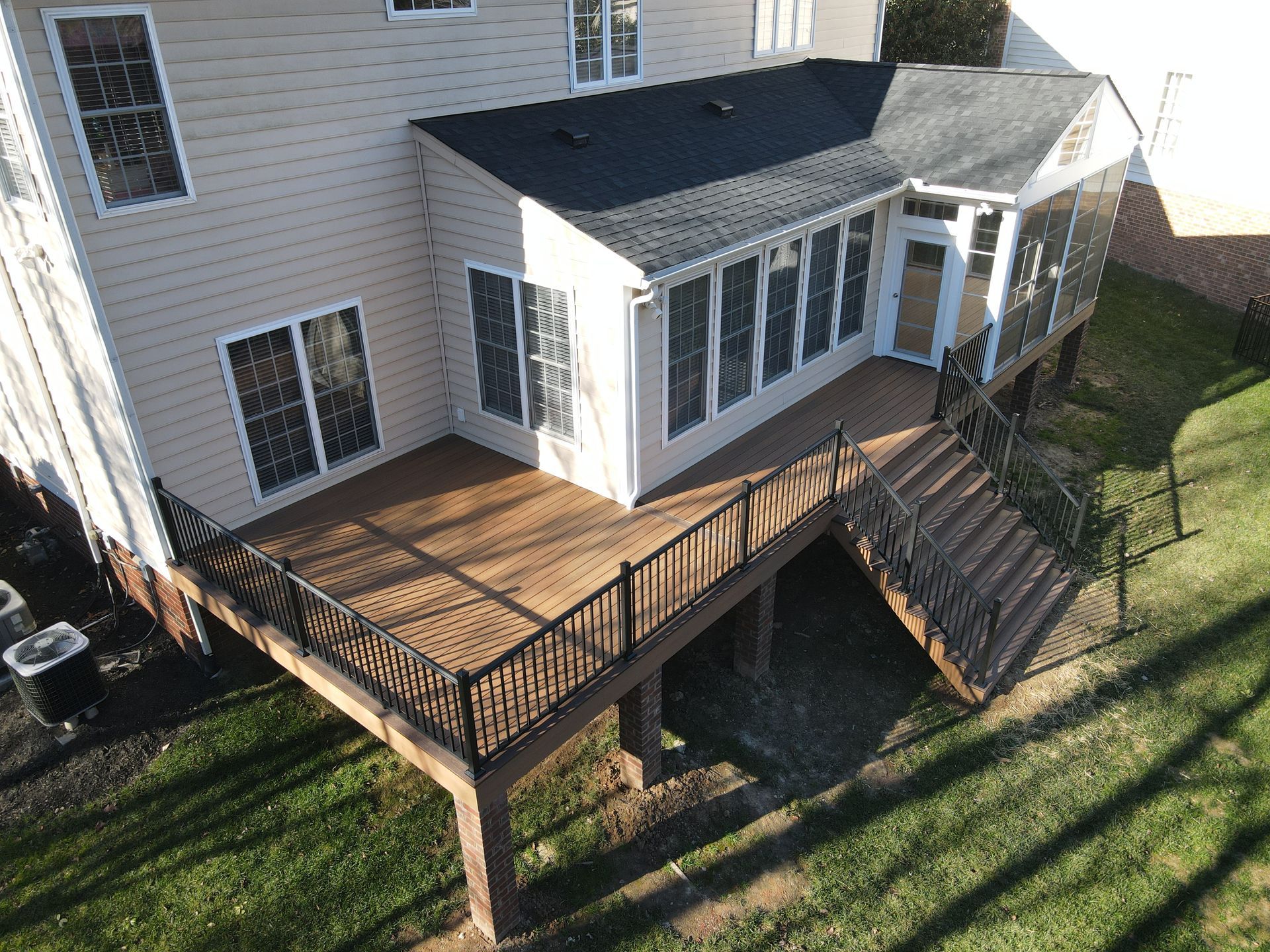 Elevated wooden deck with black railings beside a beige house, overlooking a grassy backyard.