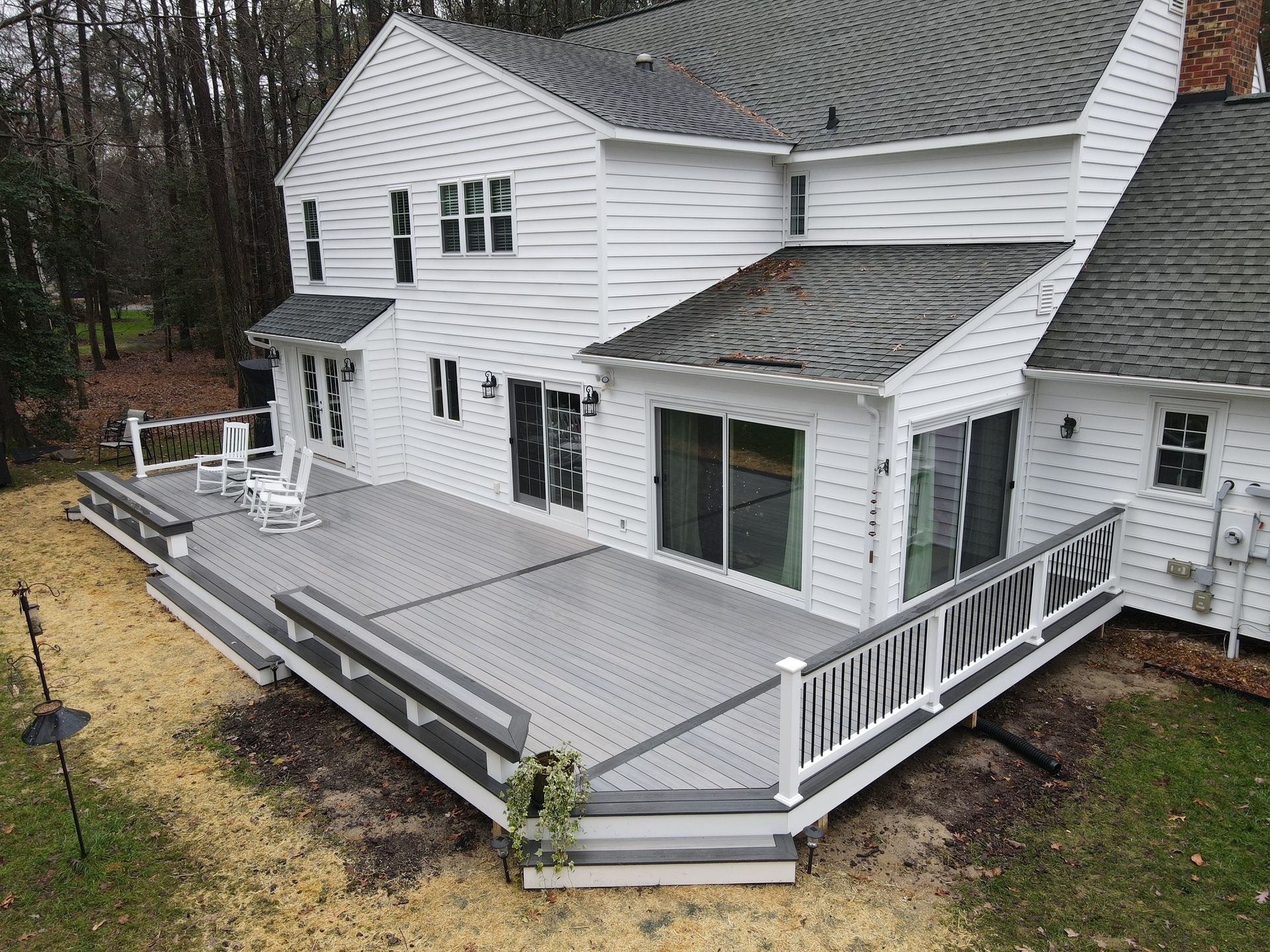 White house with a large gray wooden deck and white railing on a wooded hillside