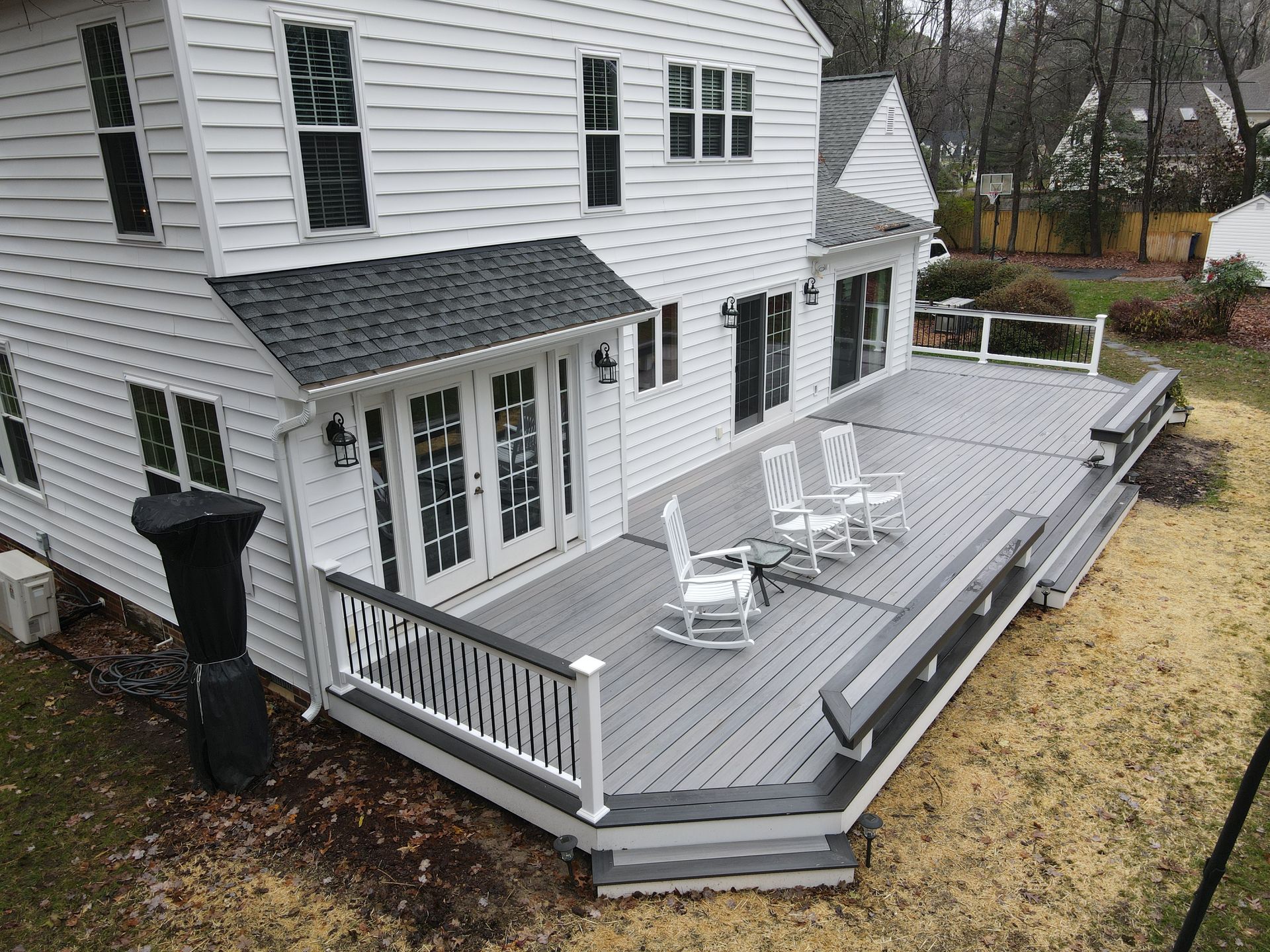 White two-story house with a large gray deck and white patio chairs in a wet yard