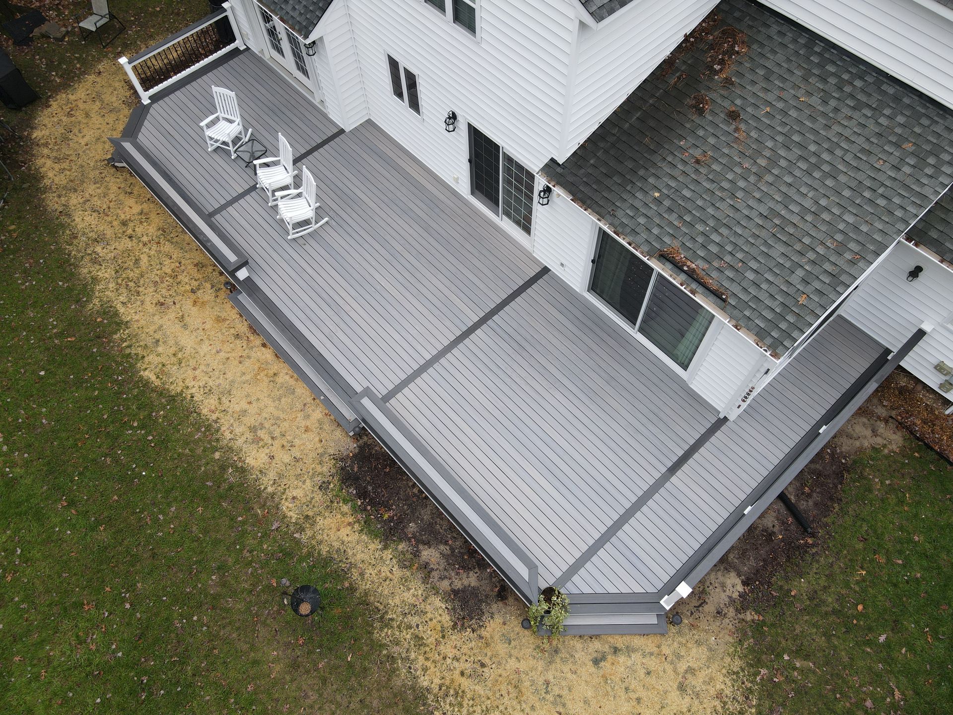 Aerial view of a house with a large gray wooden deck and white patio chairs in the backyard.