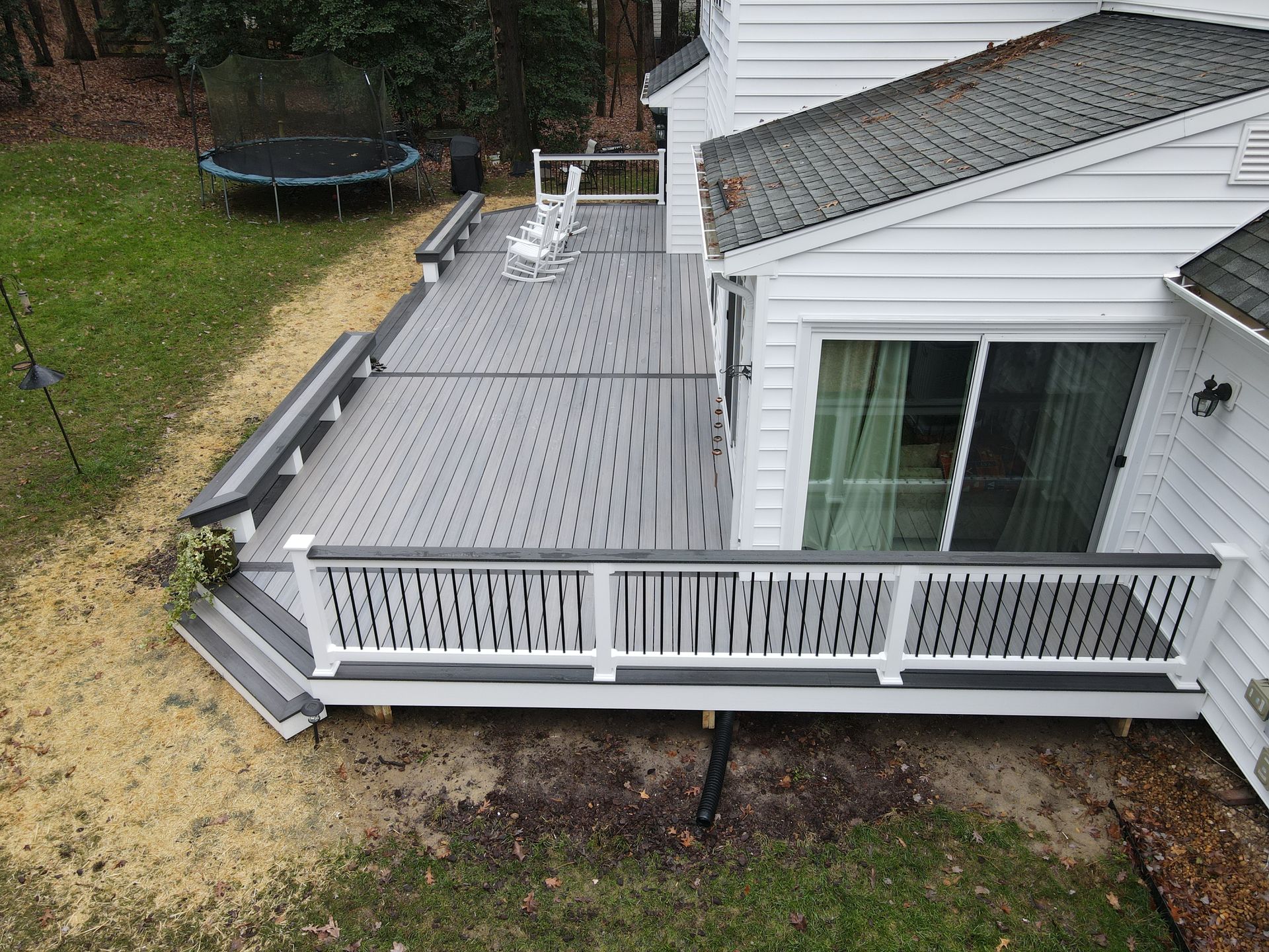 Backyard deck with gray railings and white siding beside a house, with steps leading down to the yard
