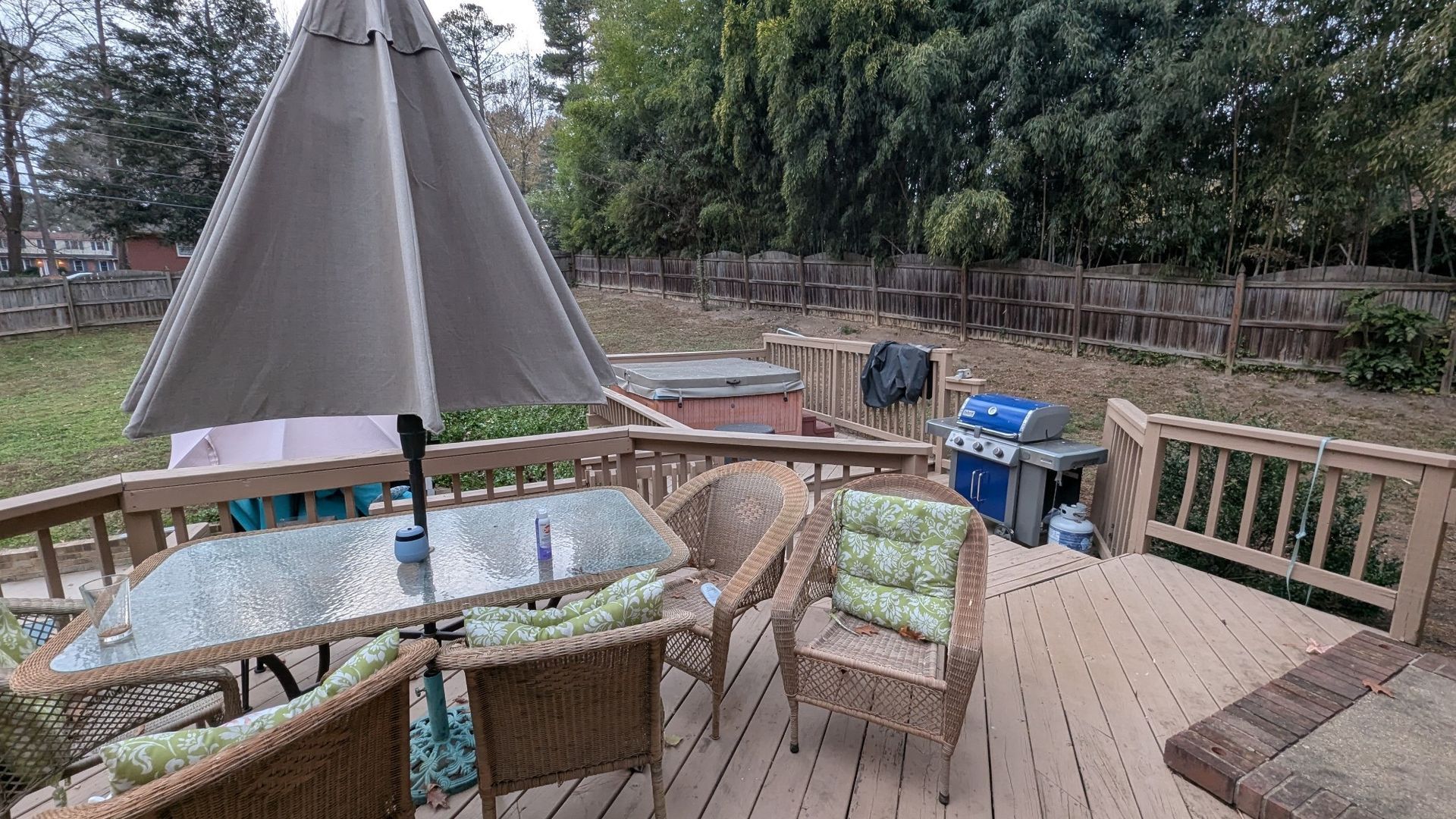 Wooden deck with patio table, umbrella, chairs, and a hot tub overlooking a fenced yard.
