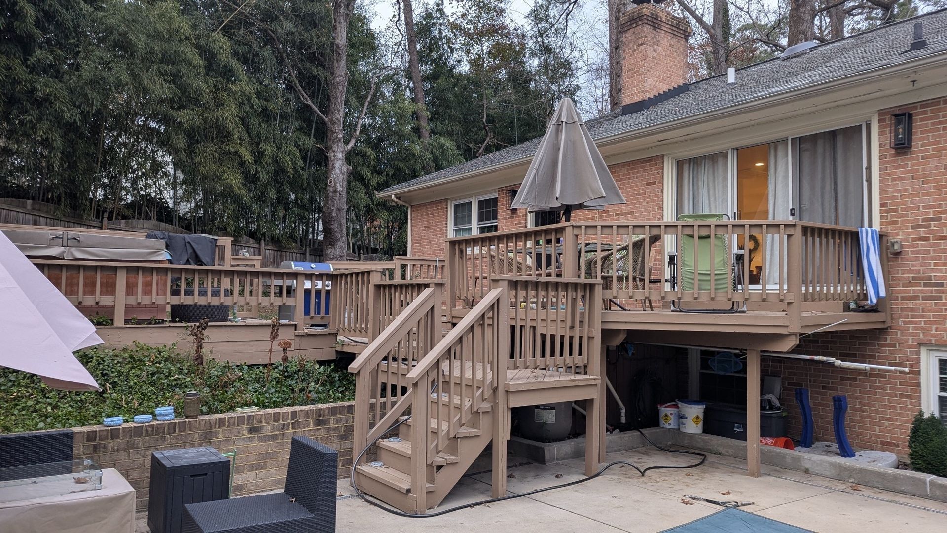 Backyard deck with wooden stairs, patio furniture, and a brick house at dusk