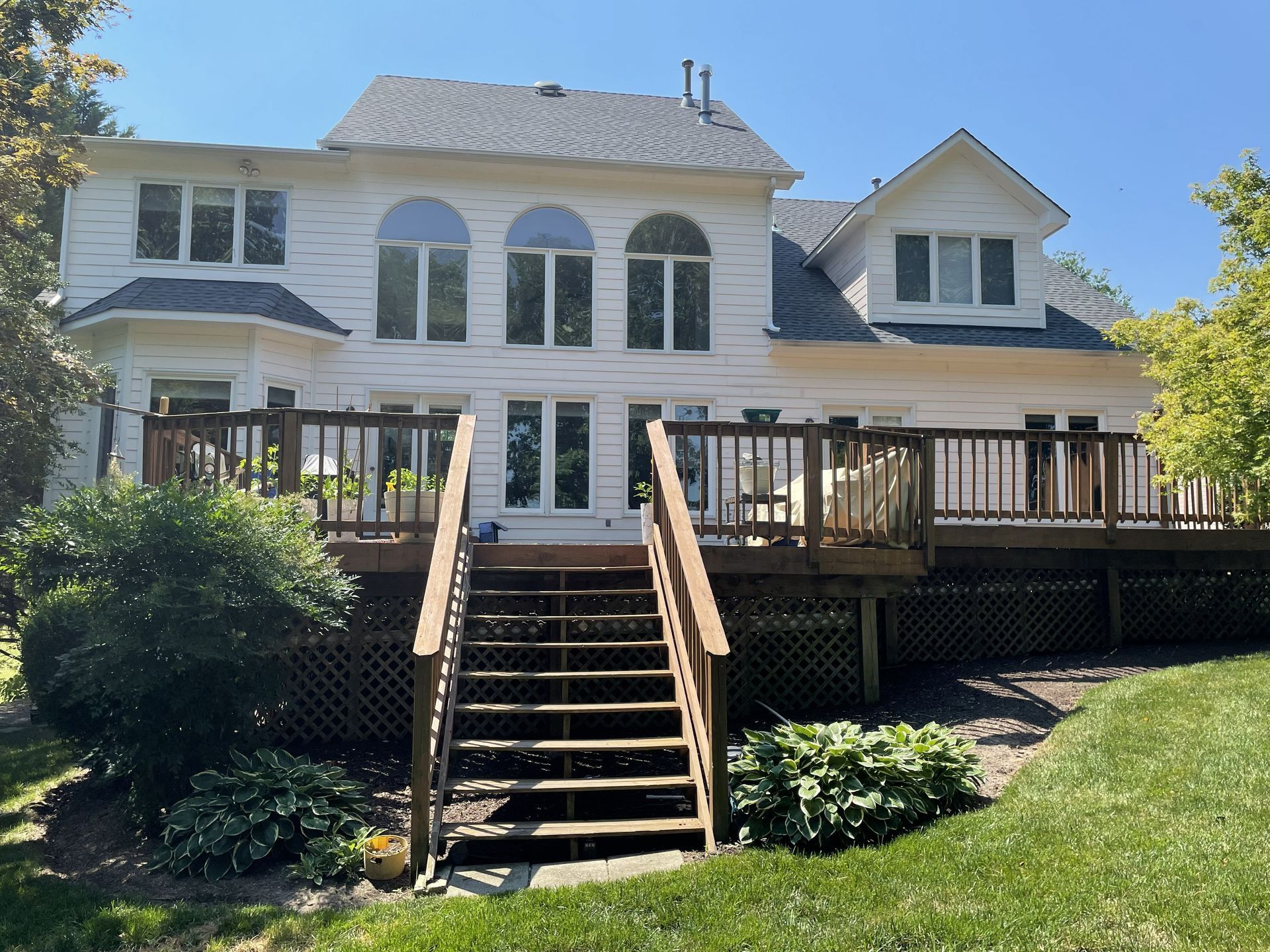 Backyard view of a white house with a raised wooden deck and central staircase leading to the lawn