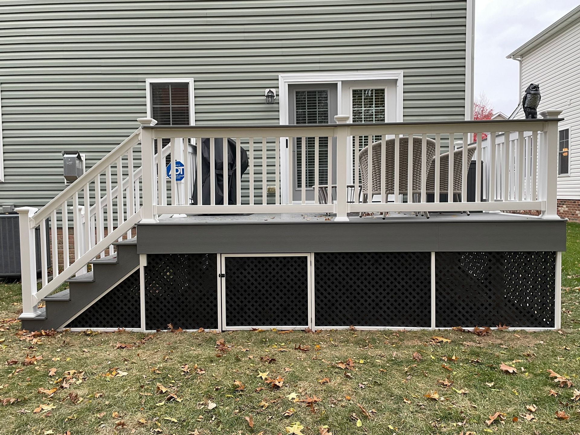 Backyard deck with white railing, stairs, and lattice skirting against a gray house.