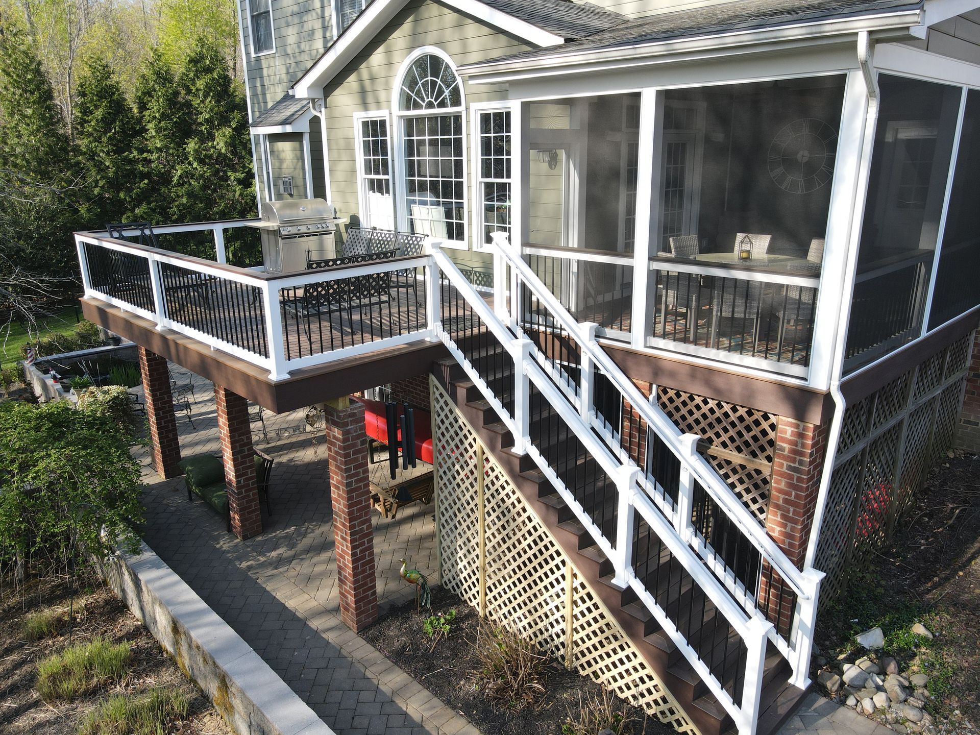 Raised house deck with white railings and screened porch above a brick foundation