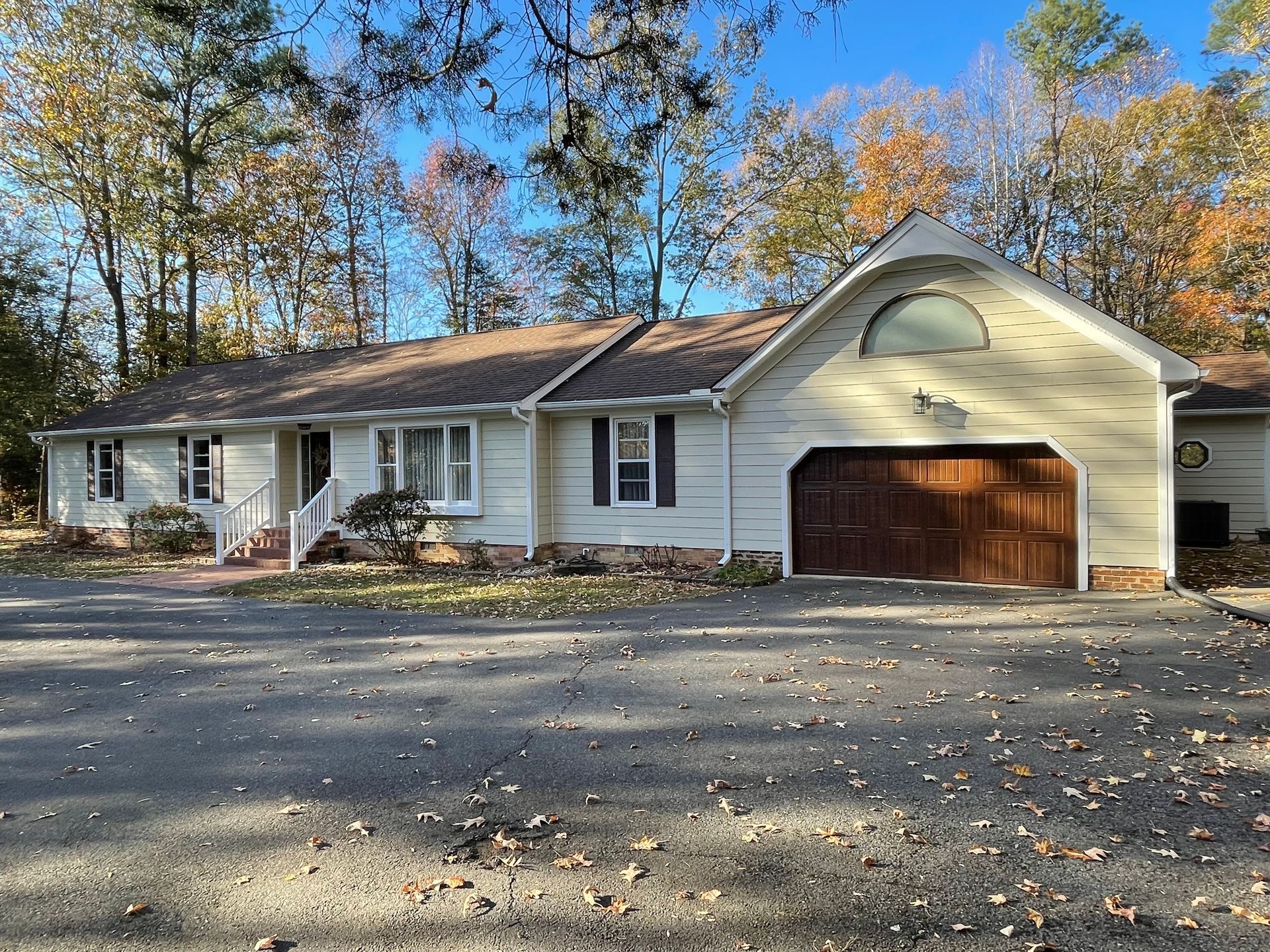 Single-story white house with brown garage and autumn trees behind it