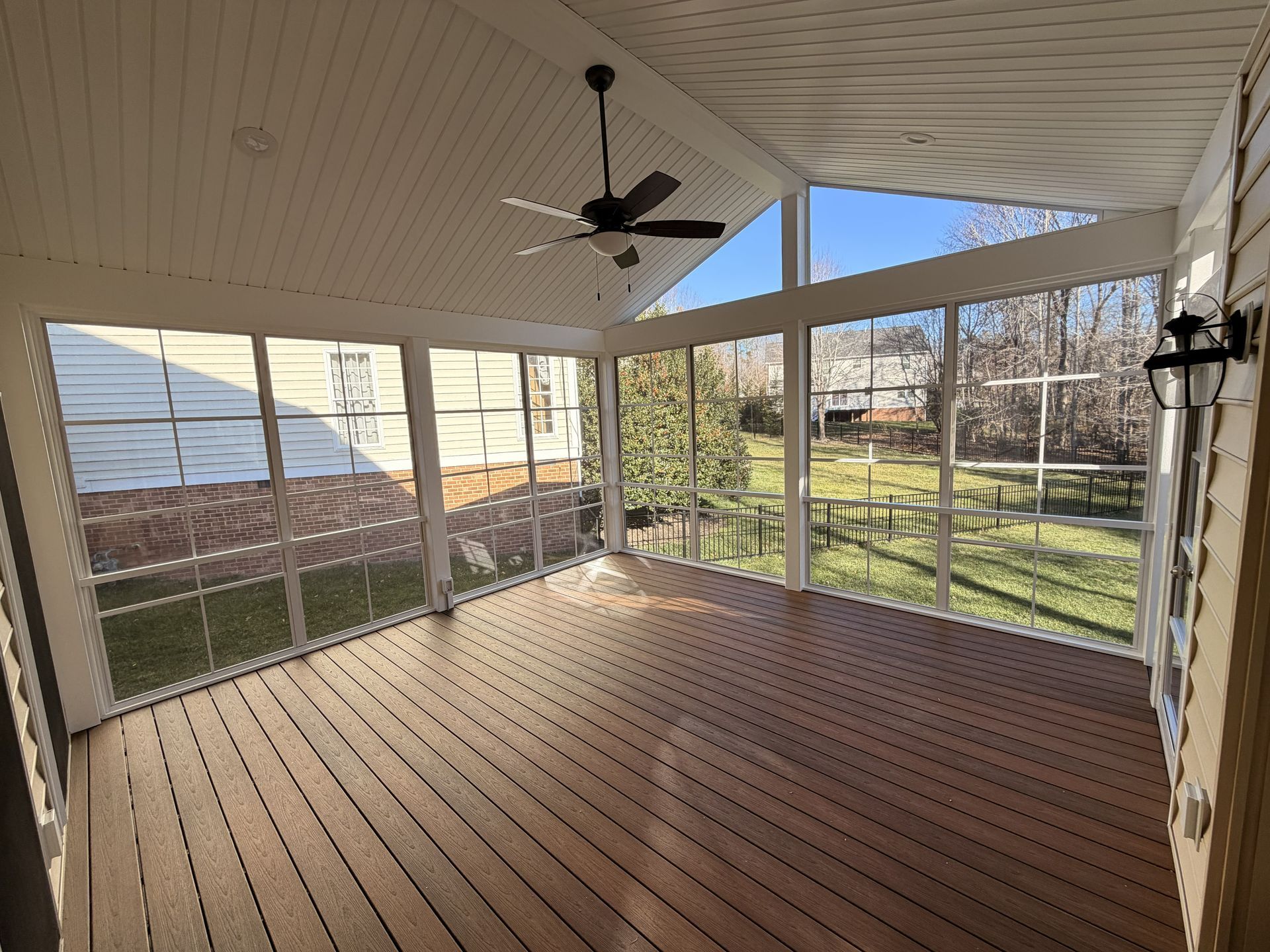 Screened porch with wood floor, ceiling fan, and large windows overlooking a backyard