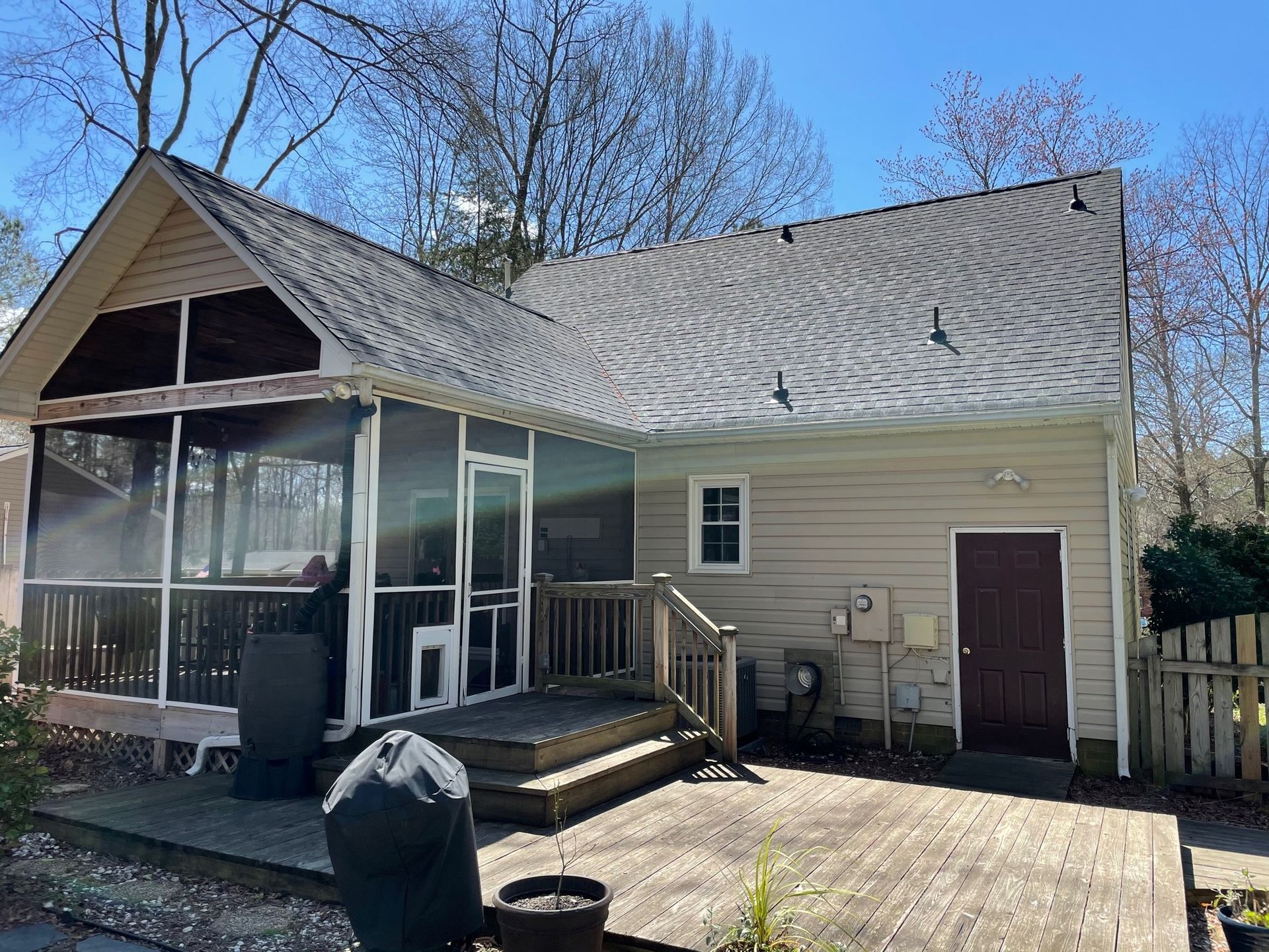 Outdoor deck beside a beige house with screened porch, white railing, and a dark grill in the foreground