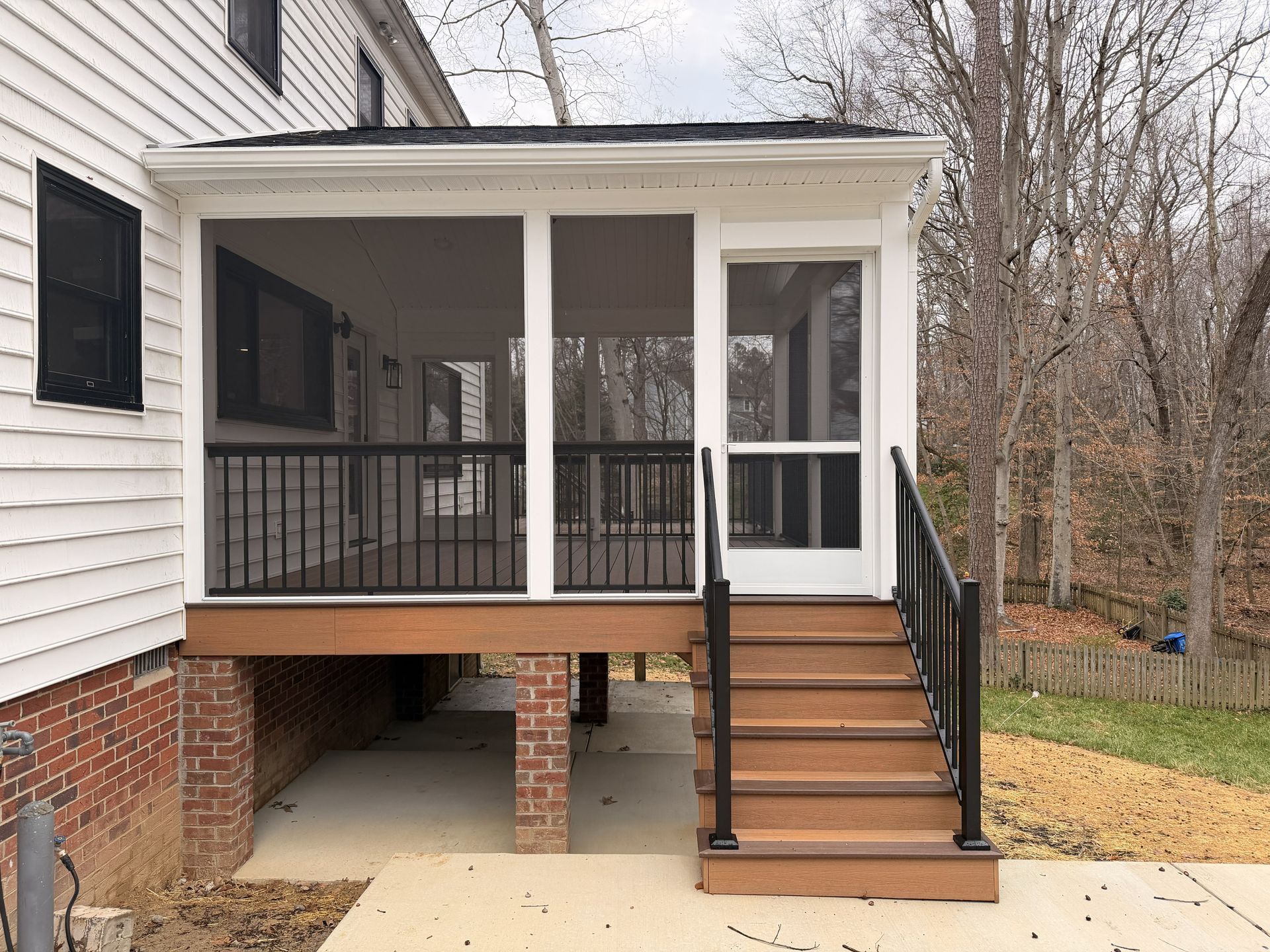 Back porch with screened-in deck, brown stairs, and black railings on a white house.
