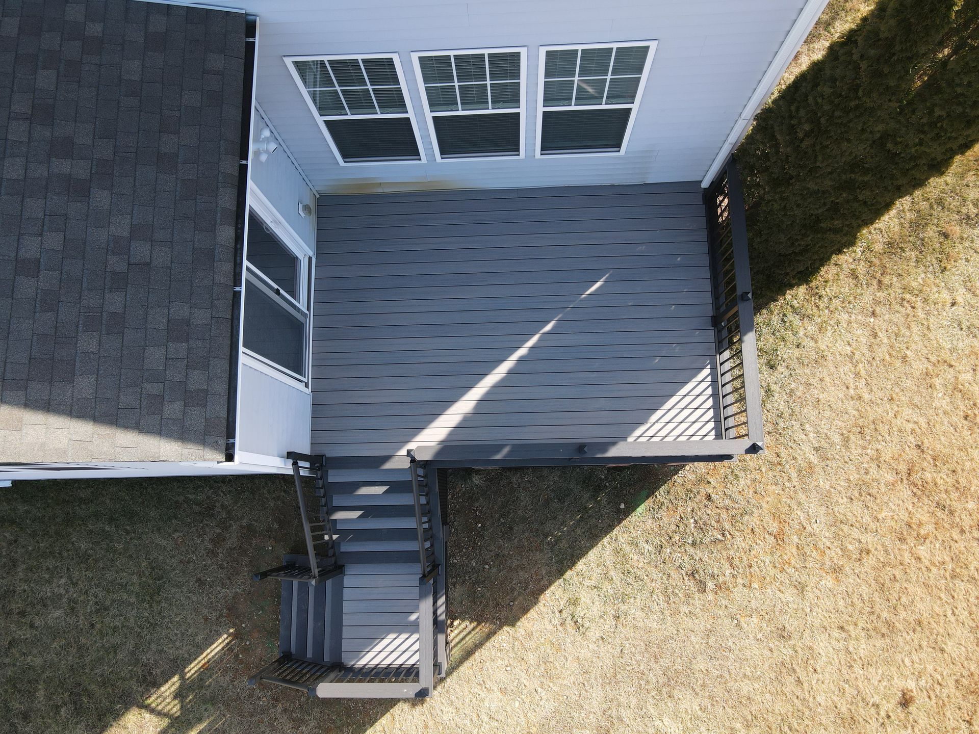 Overhead view of a gray deck with stairs, white doors, and a grassy yard beside a house
