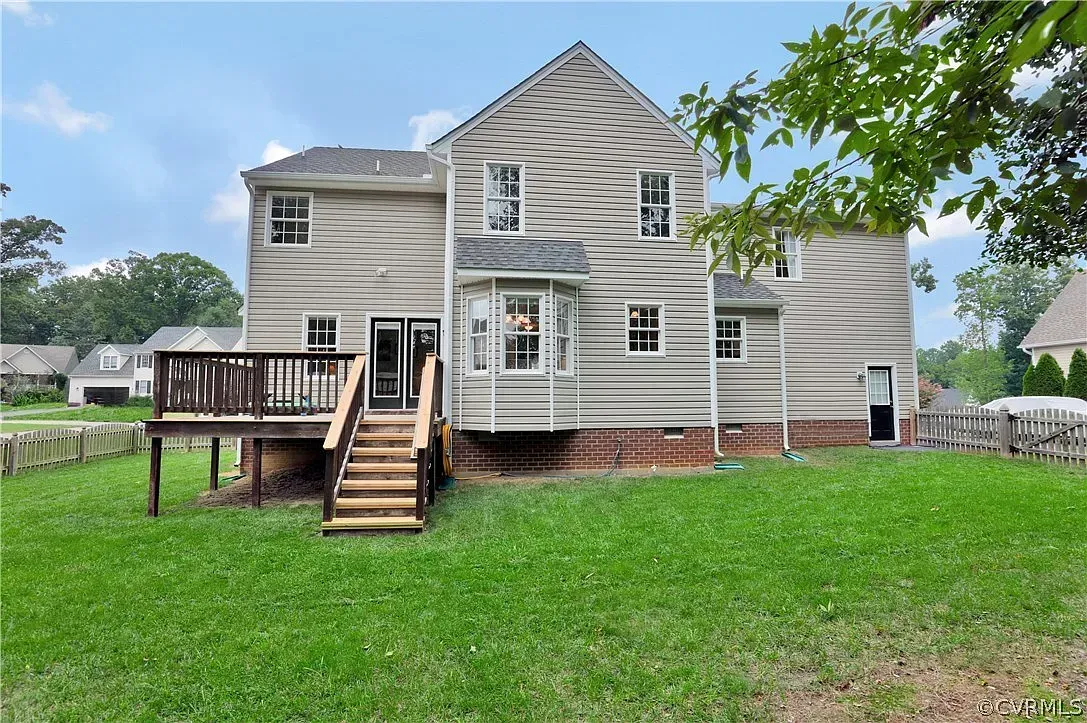 Backyard view of a weathered gray house with a raised deck and stairs leading to a grassy yard