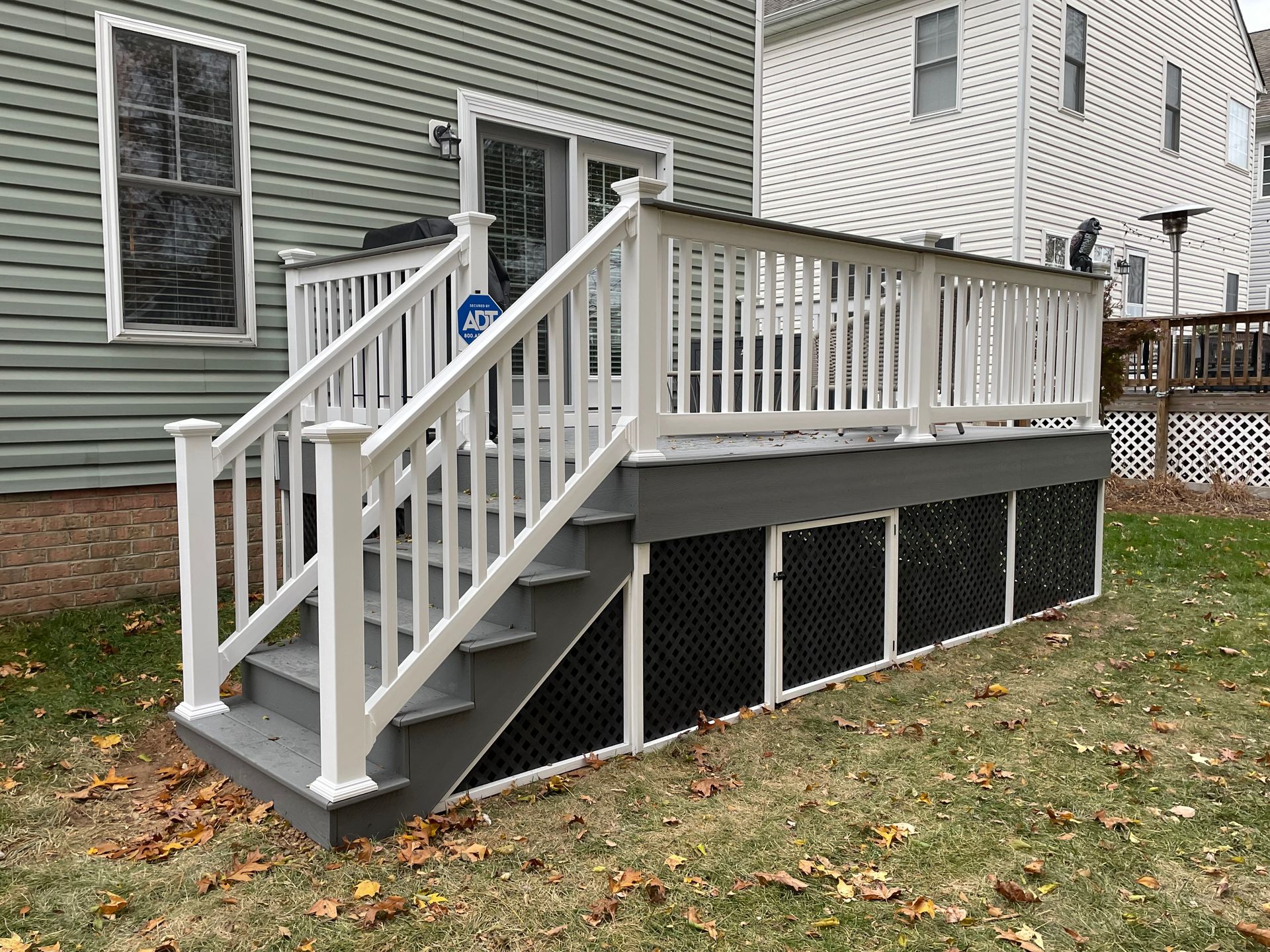 White wooden deck stairs with railing on a house’s side yard, raised over a gravel-covered lower area.