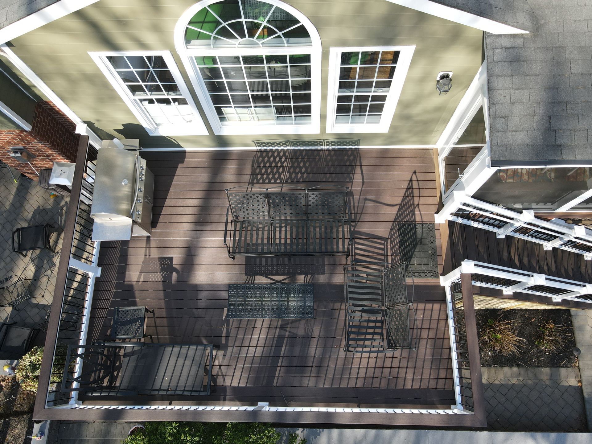 Overhead view of a backyard patio with black metal furniture, white house siding, and surrounding deck rails