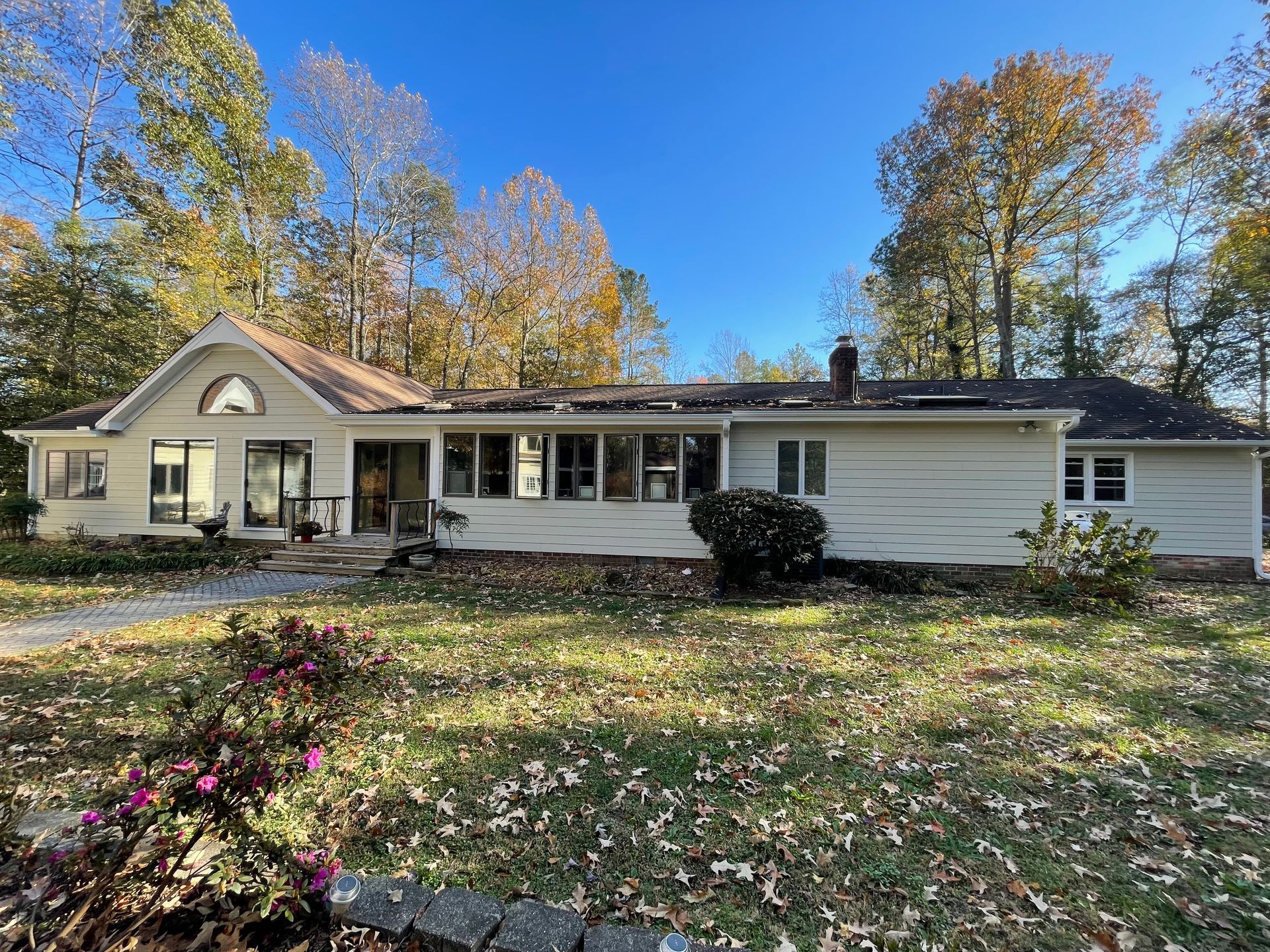 Single-story beige house with a front porch, autumn trees, and a lawn covered in fallen leaves.