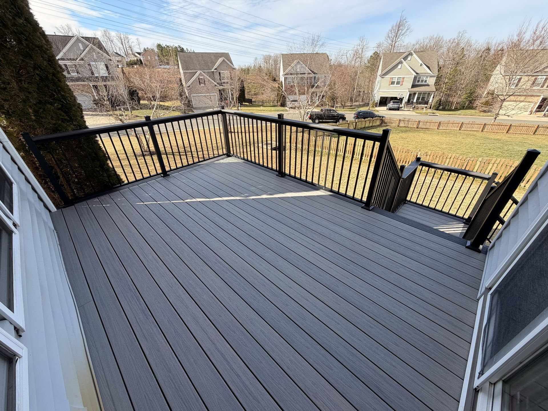 Empty gray deck with black railing overlooking a suburban yard and houses