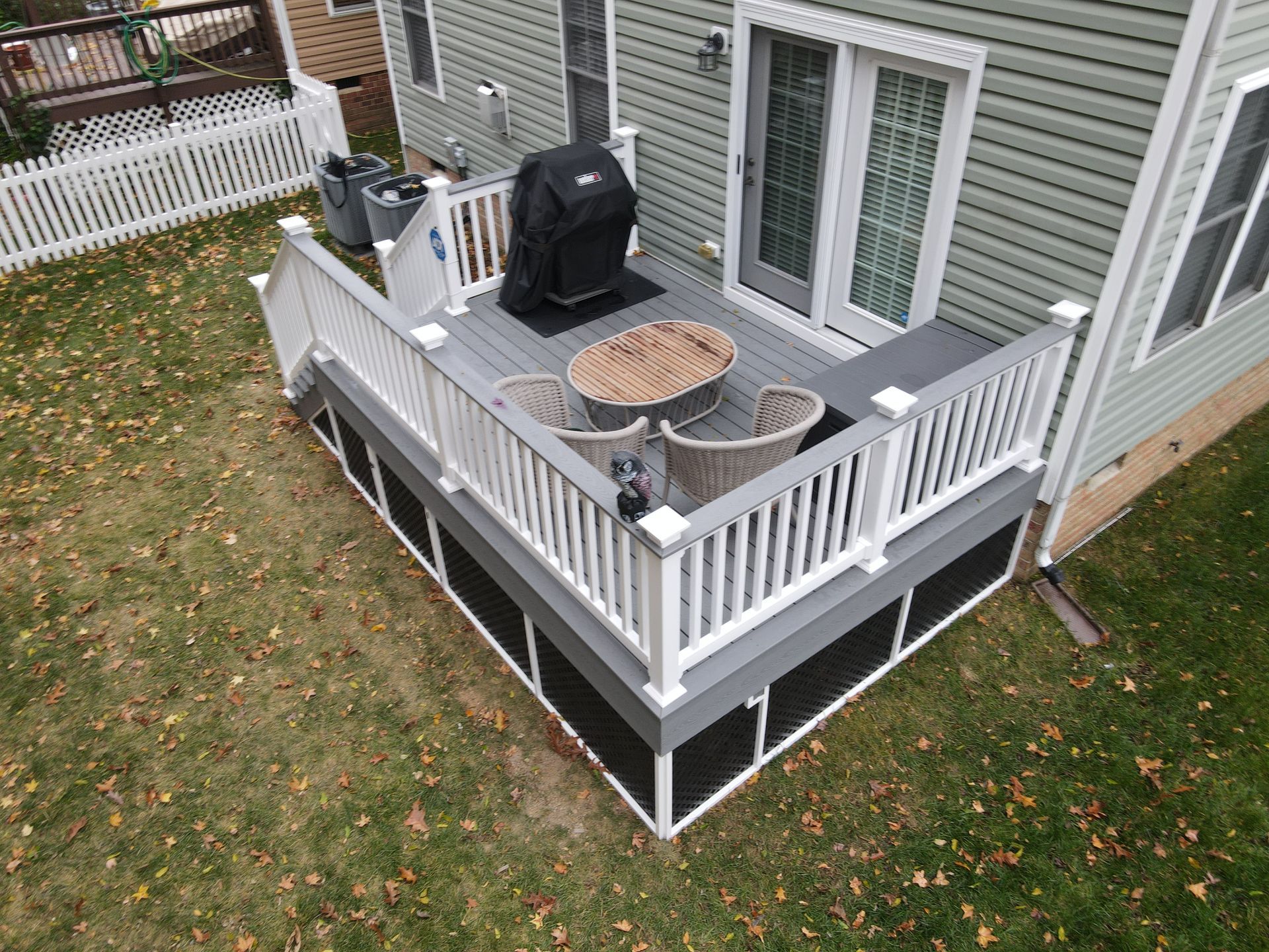 Raised gray deck with white railing, patio furniture, and a grill beside a house.