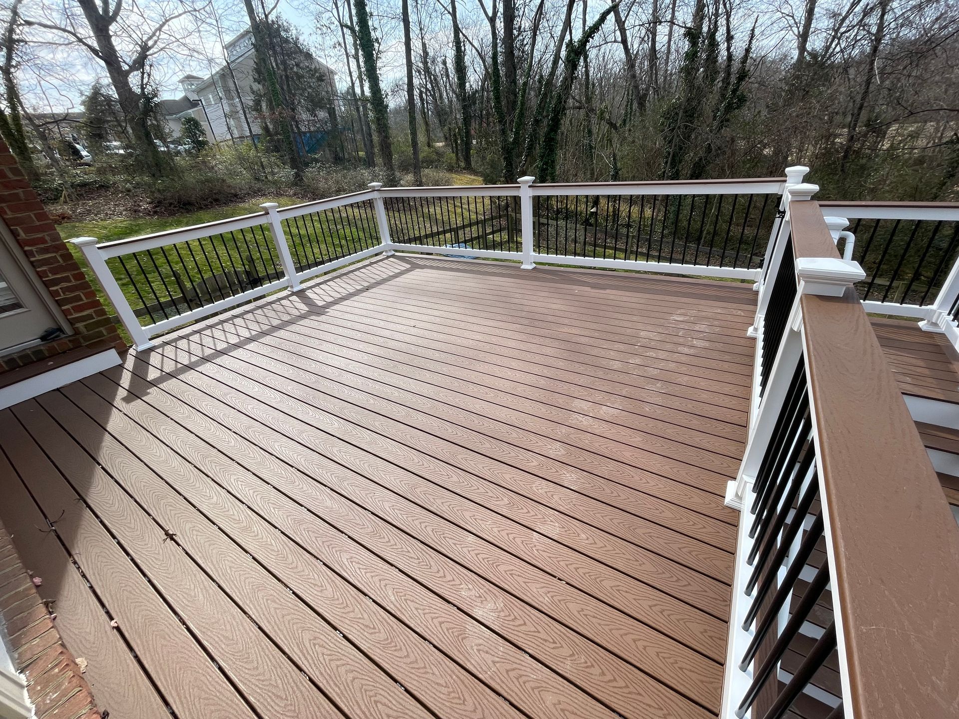 Wooden deck with white railing overlooking leafless trees and a wooded yard