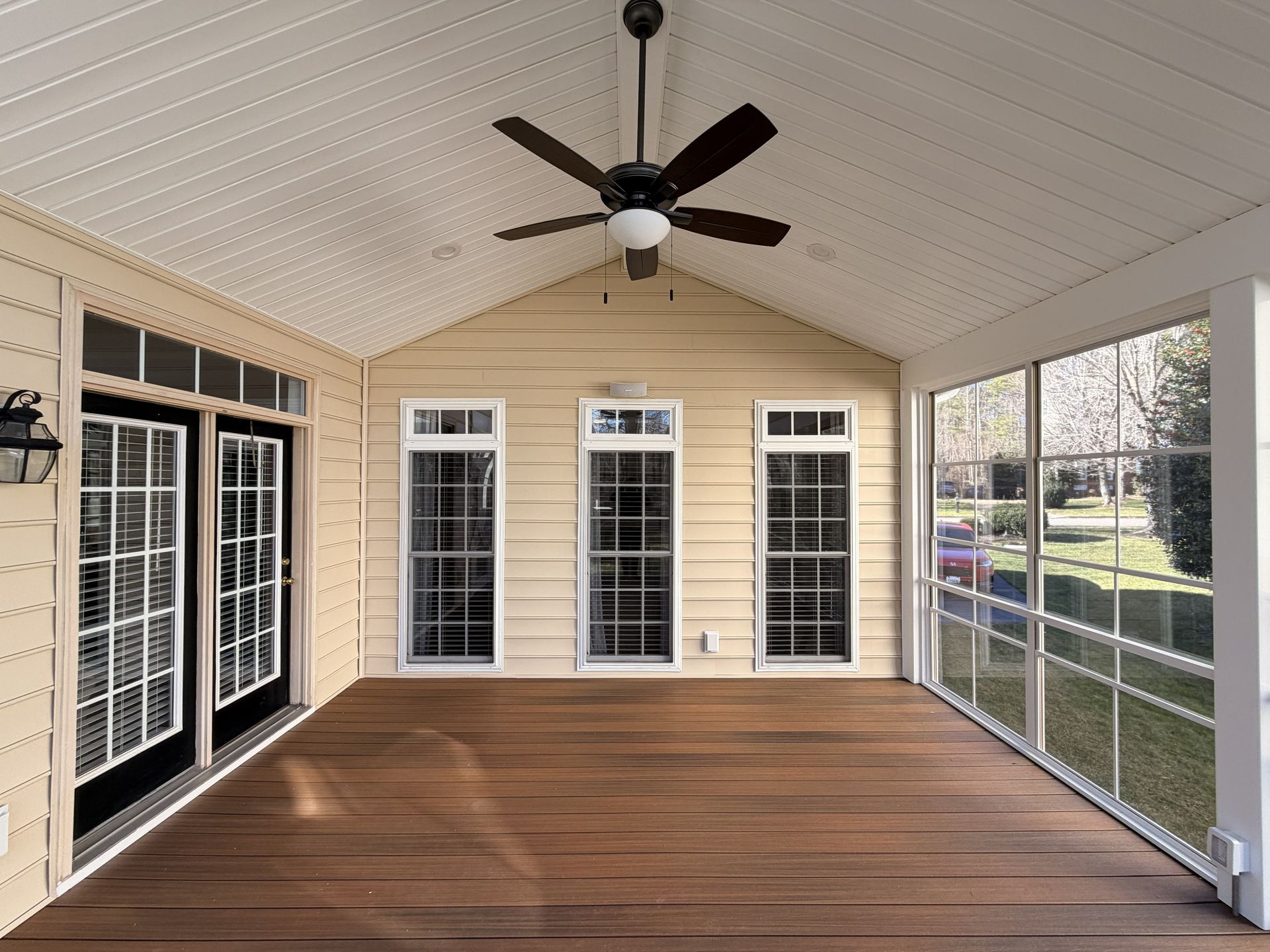 Covered screened-in porch with wood floor, ceiling fan, and large windows overlooking a yard.
