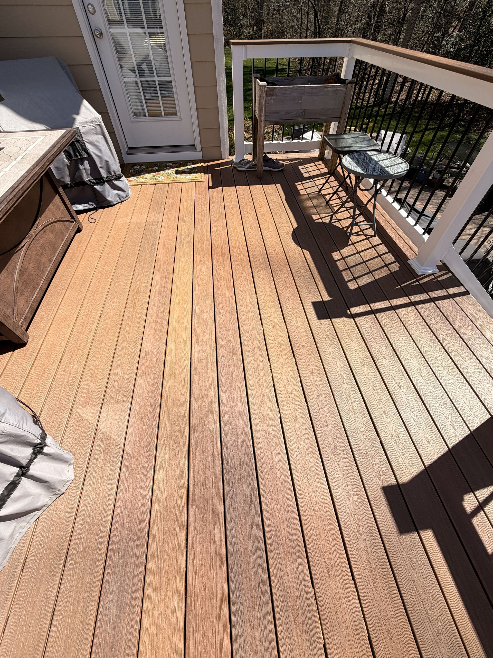 Wooden deck with white railings, a sliding door, and sunlight casting shadows.