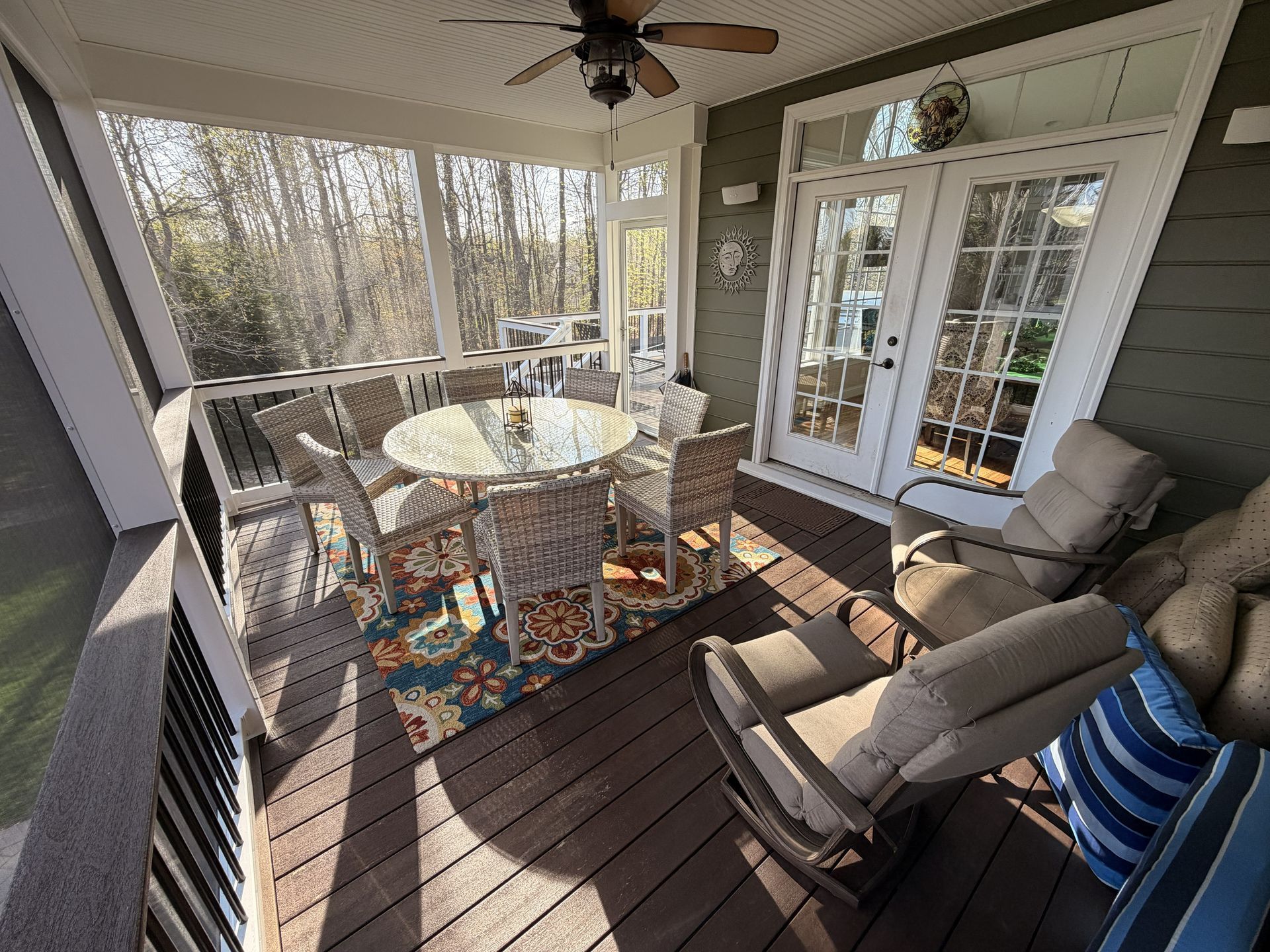 Covered porch with round table, cushioned chairs, and glass French doors overlooking trees