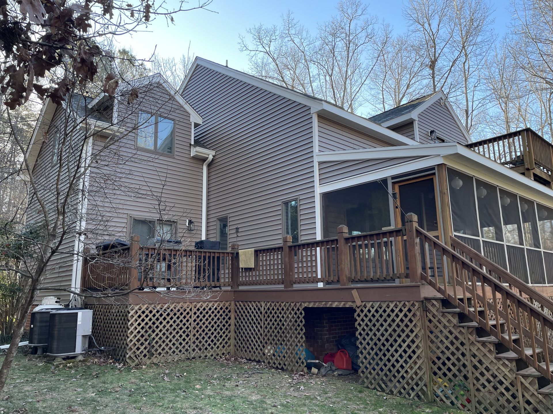 Rear view of a house with a wooden deck, lattice skirting, and stairs in a wooded yard