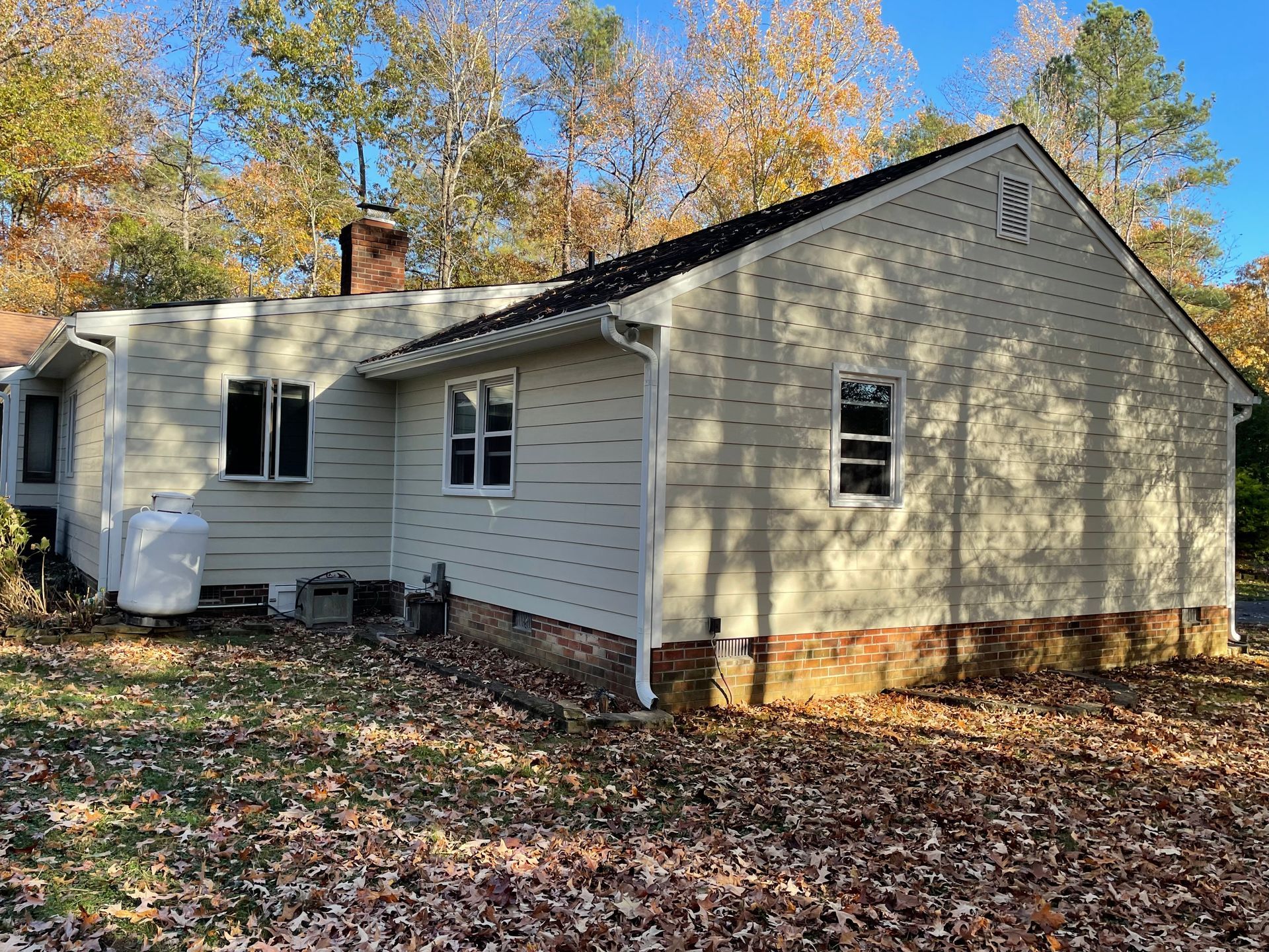 White single-story house with tan siding, screened porch, and autumn trees in the yard