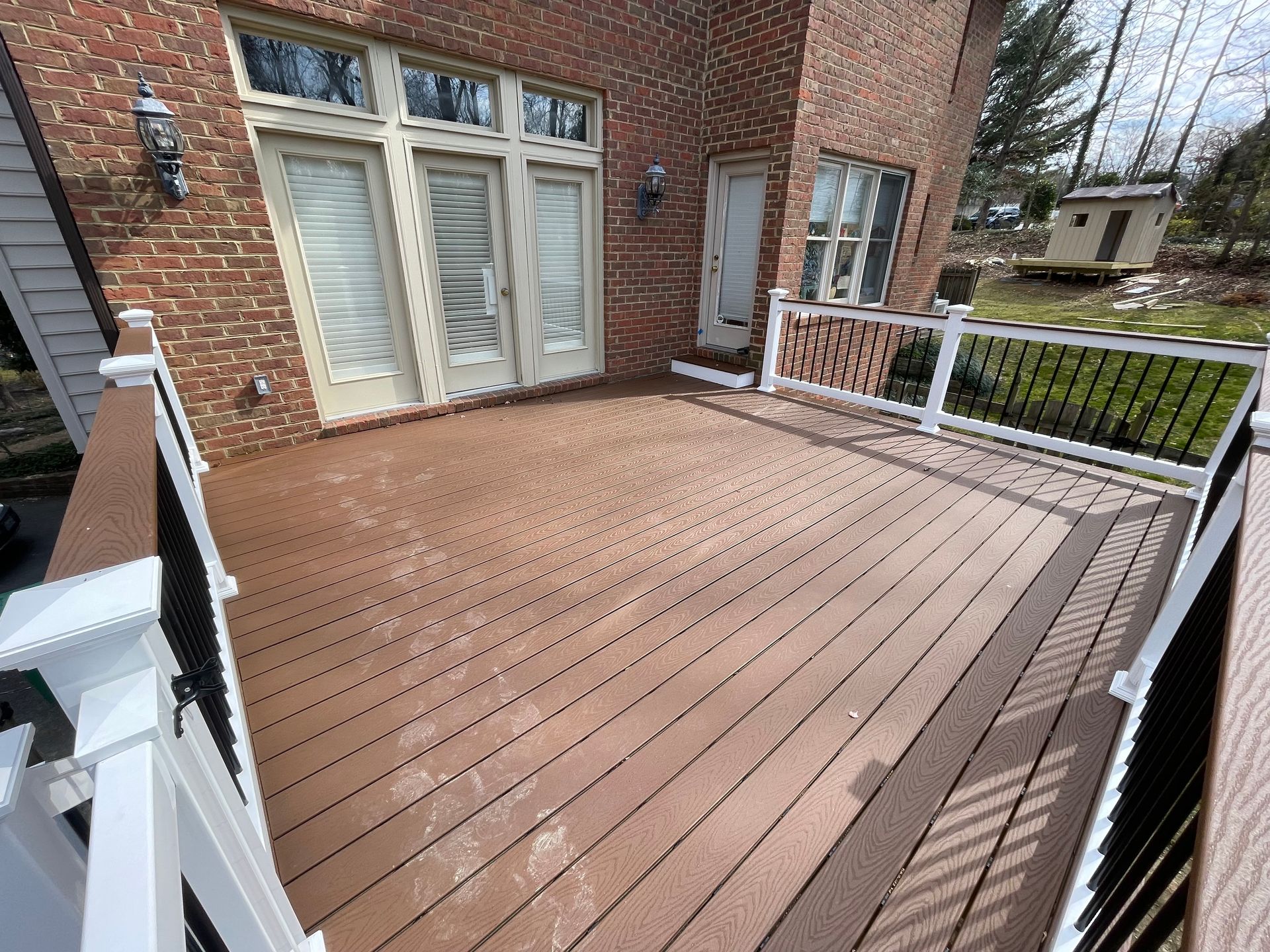 Wooden deck attached to a brick house, with white railings and a sliding glass door.