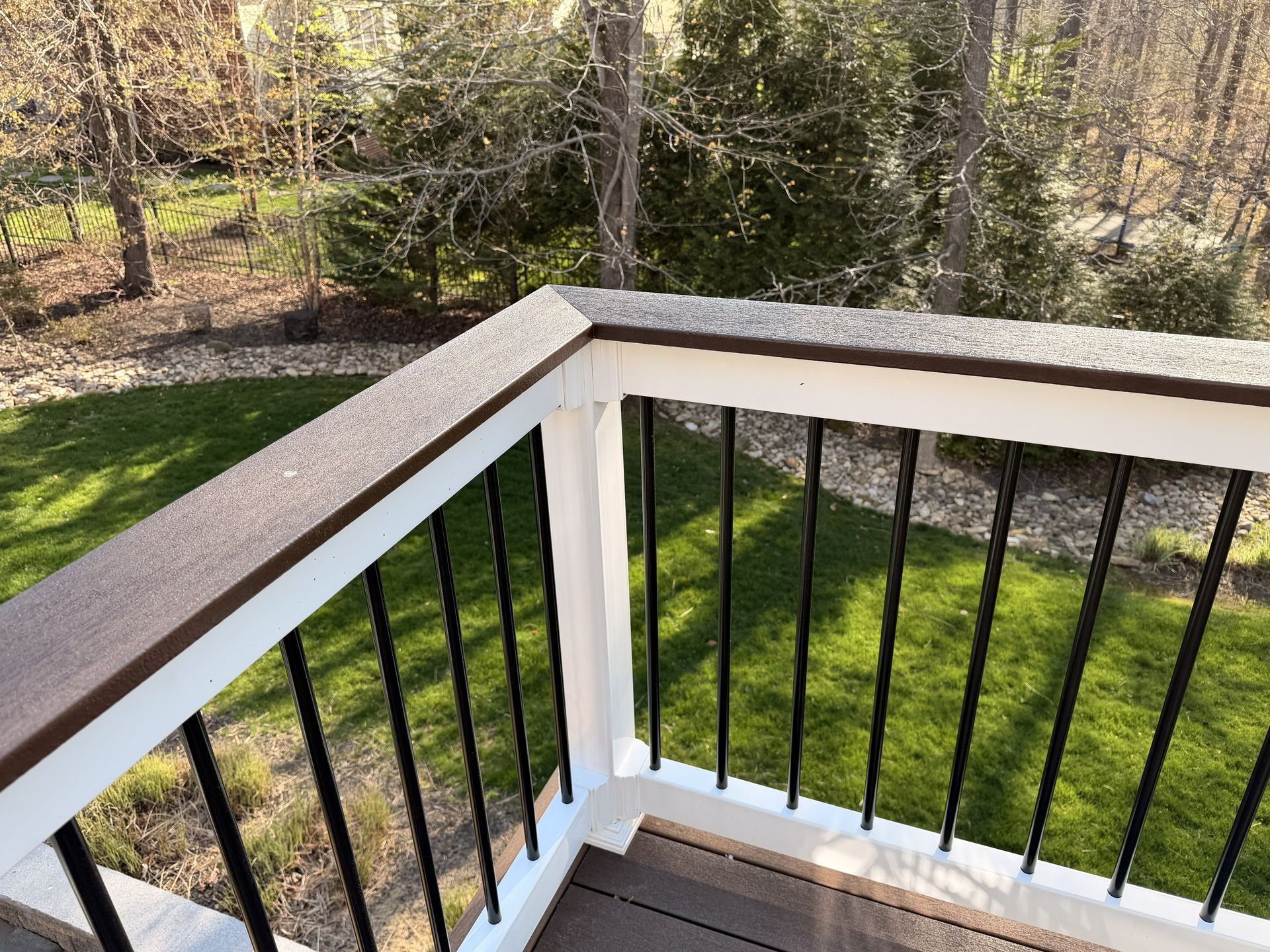White porch railing with black balusters overlooking a green backyard and wooded yard beyond