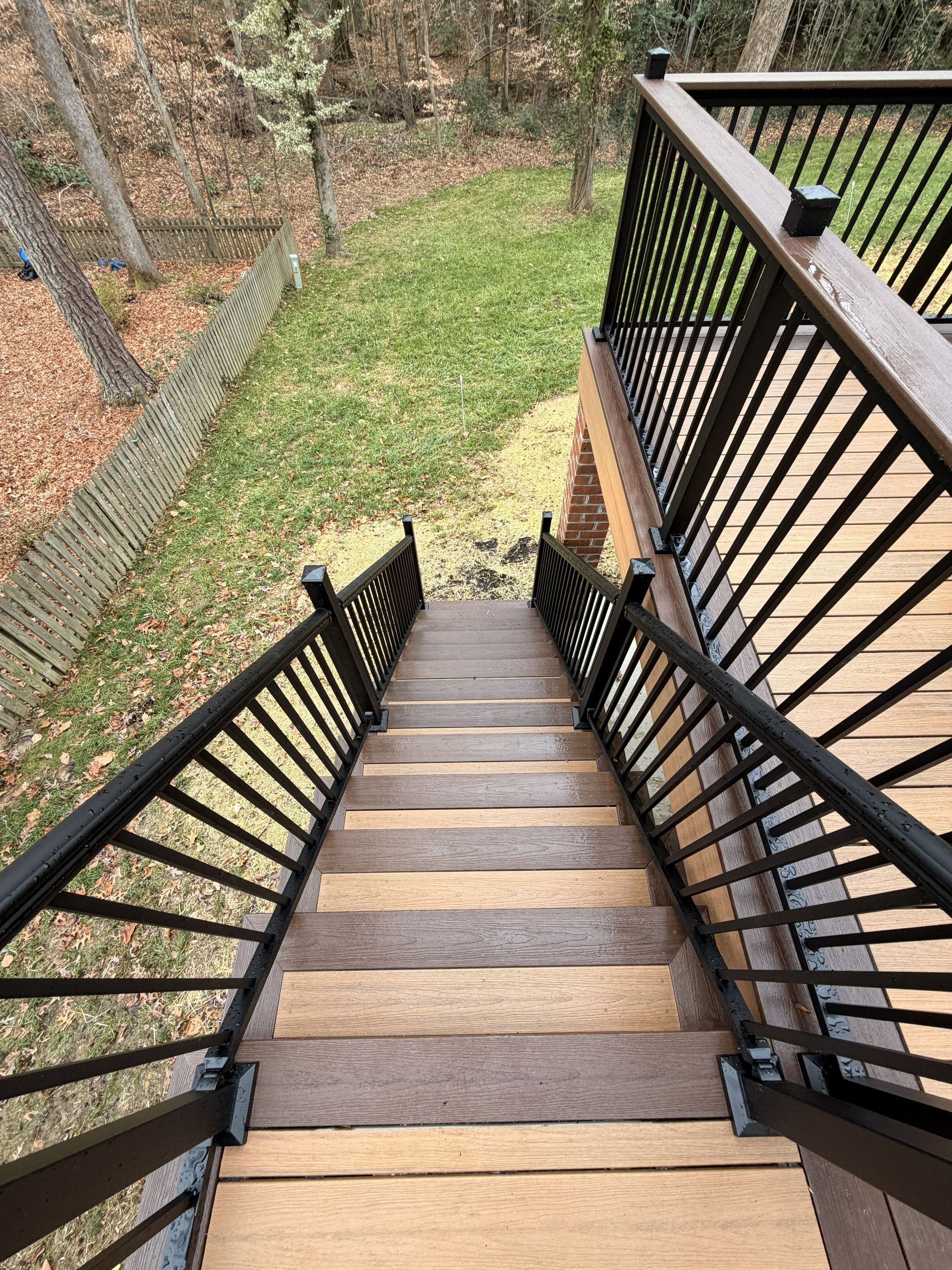 Wooden outdoor staircase with black railings descending to a grassy yard by a wooded slope