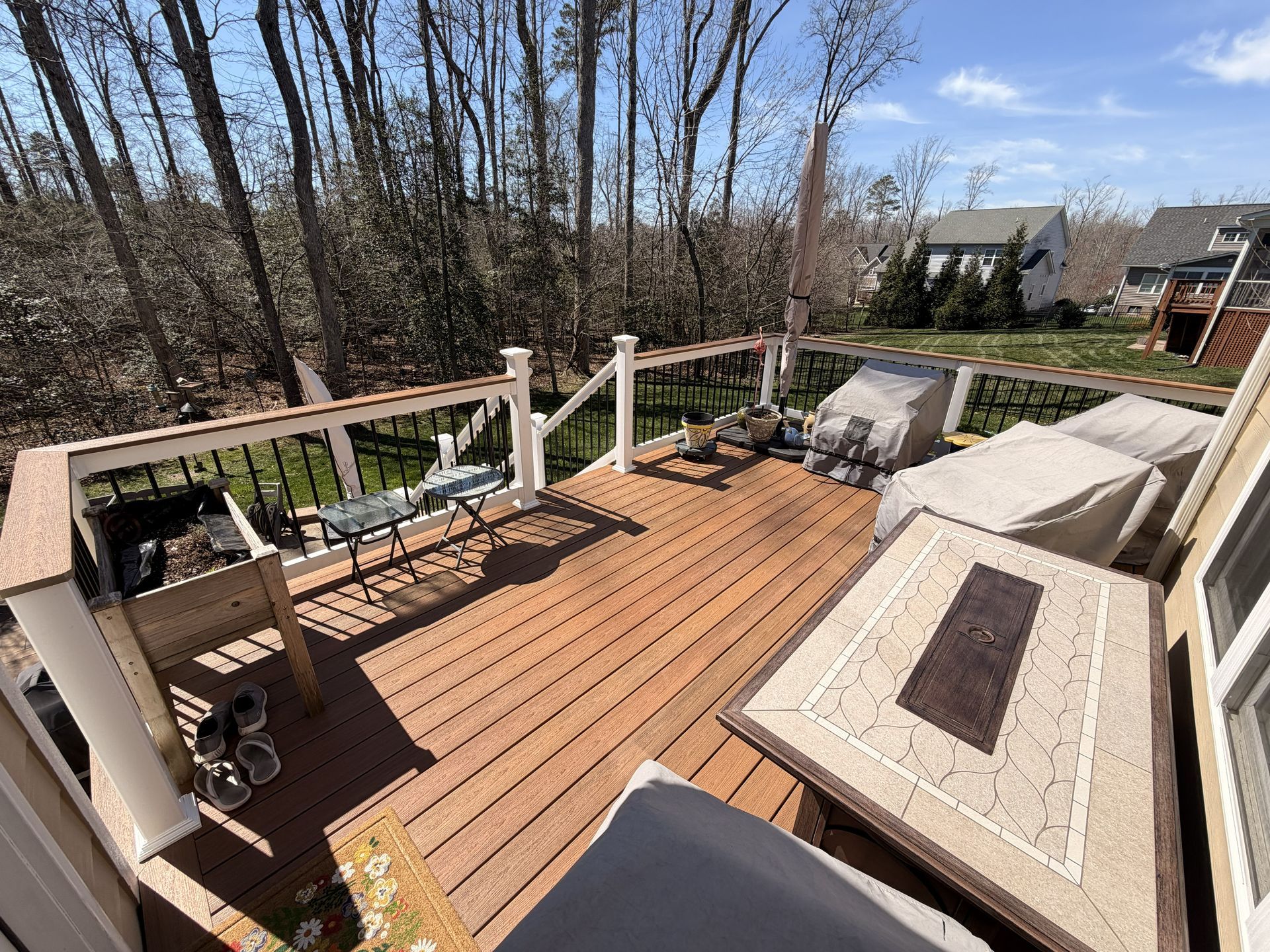 Wooden deck with white railings, outdoor seating, and leafless trees in the background