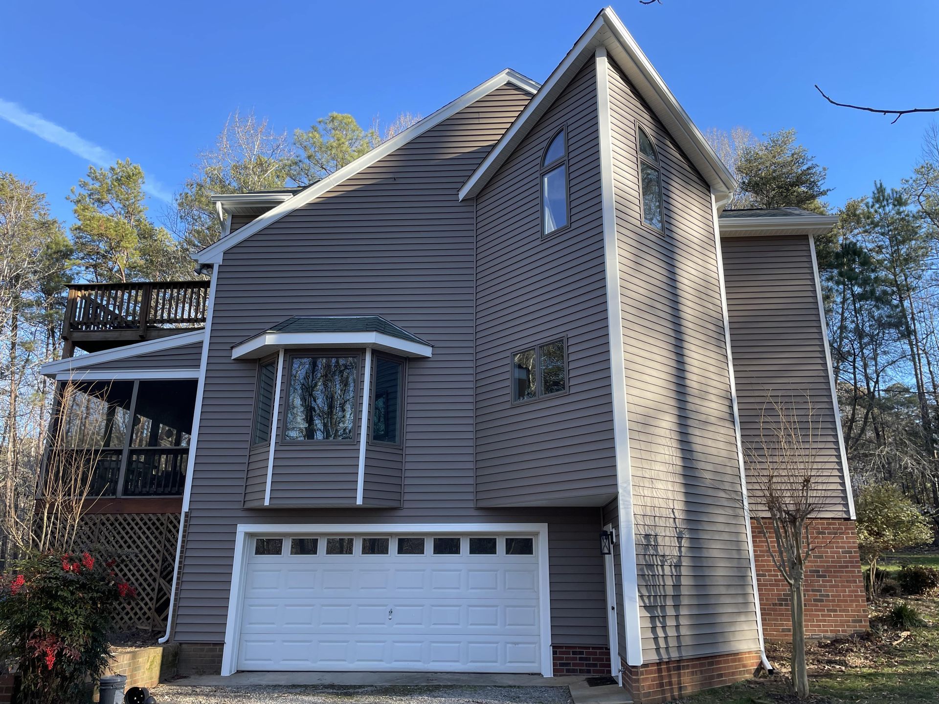 Gray two-story house with garage, white trim, and a bay window under a blue sky