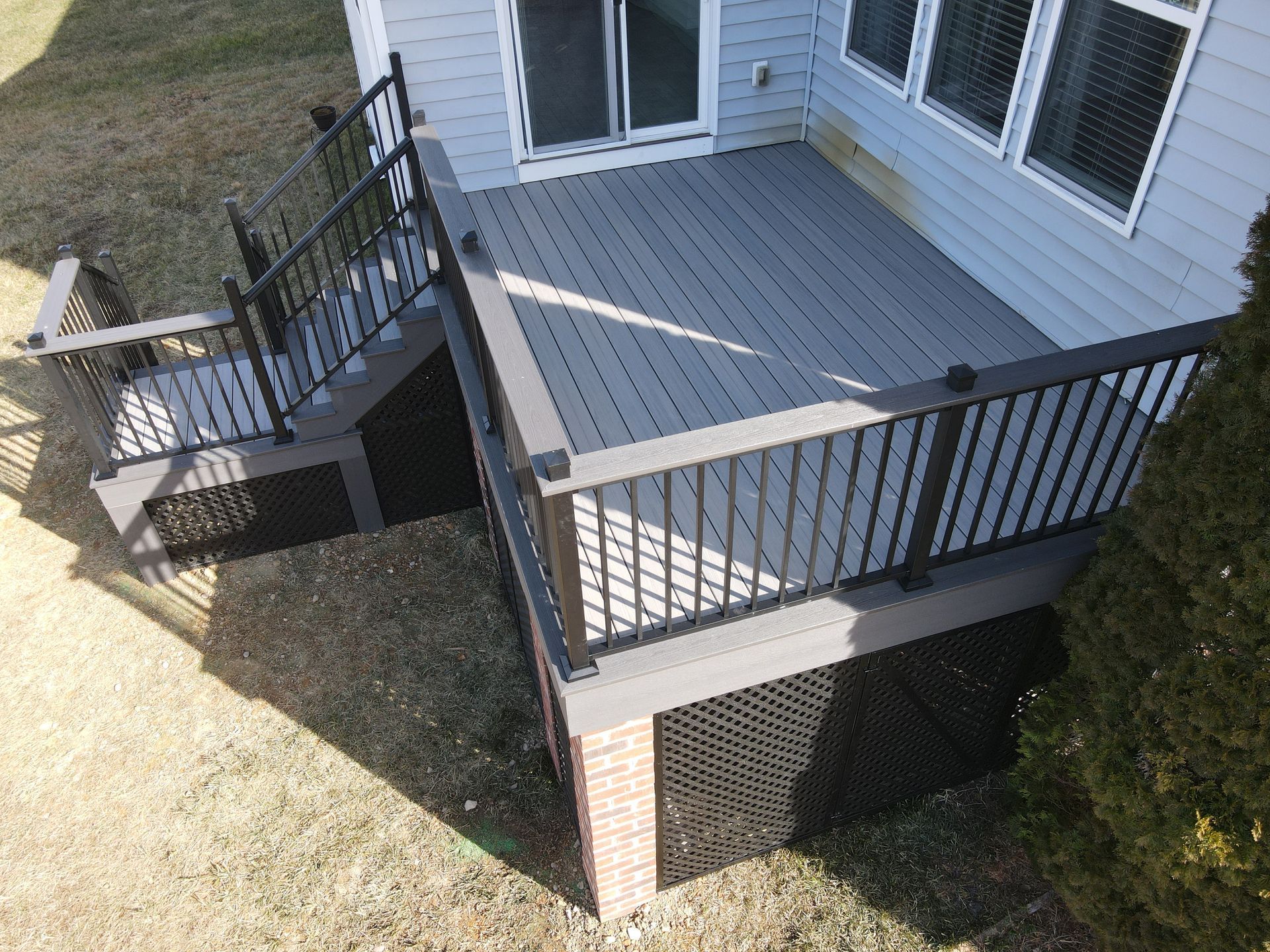 Small gray deck with black railings and steps beside a house, viewed from above