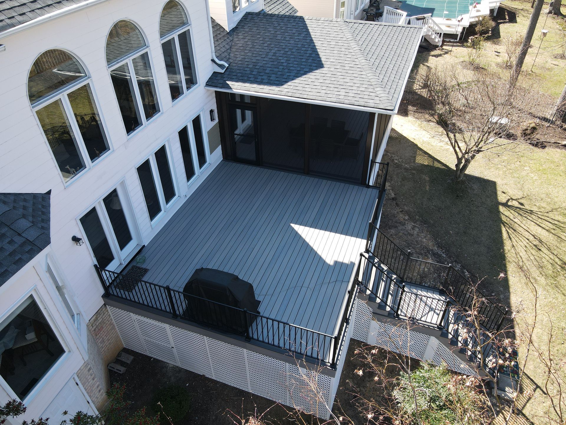 Aerial view of a white house’s backyard patio and deck with black railing and nearby trees