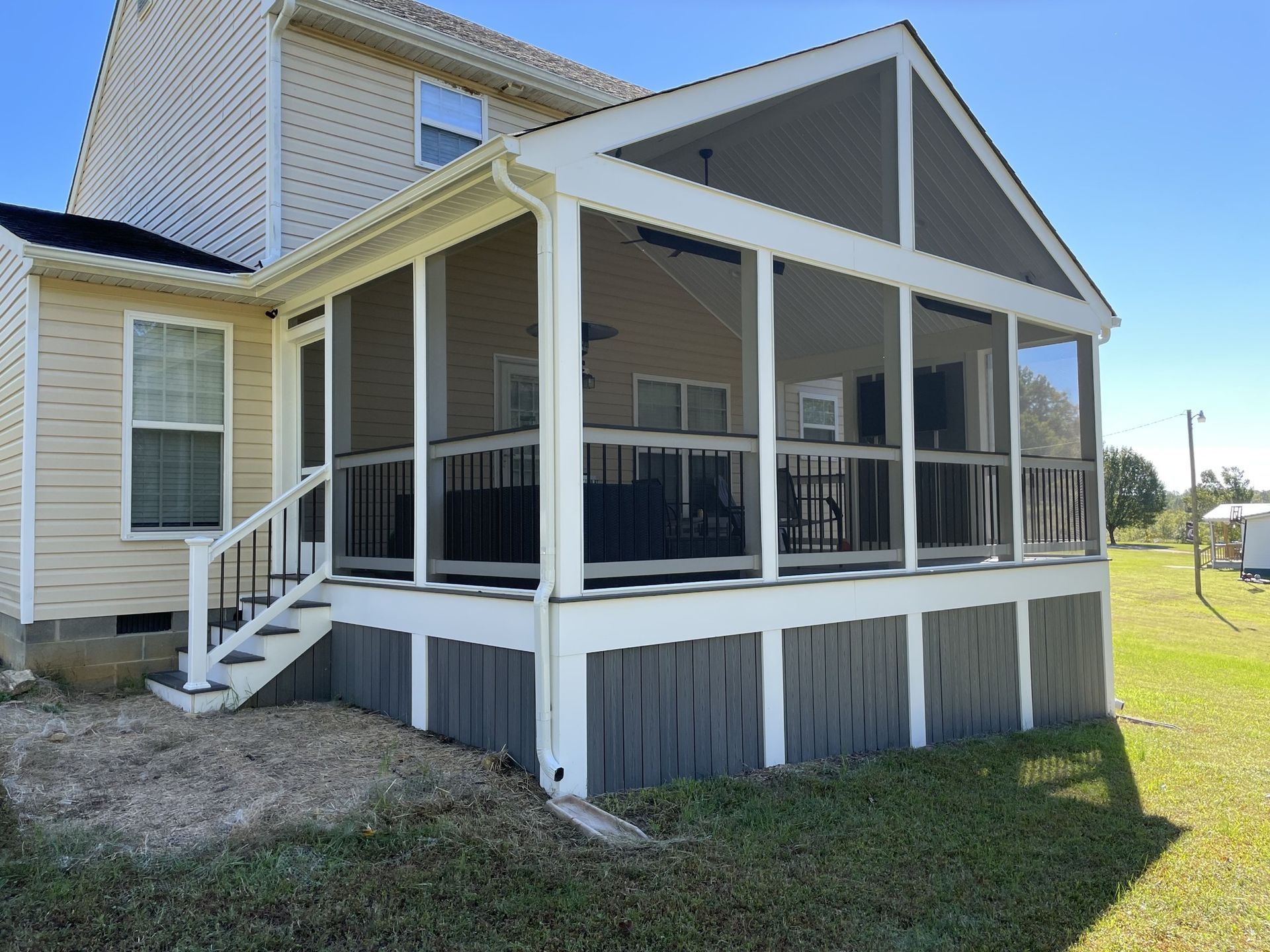 Screened porch addition on a light yellow house with white trim and gray railing under a peaked roof