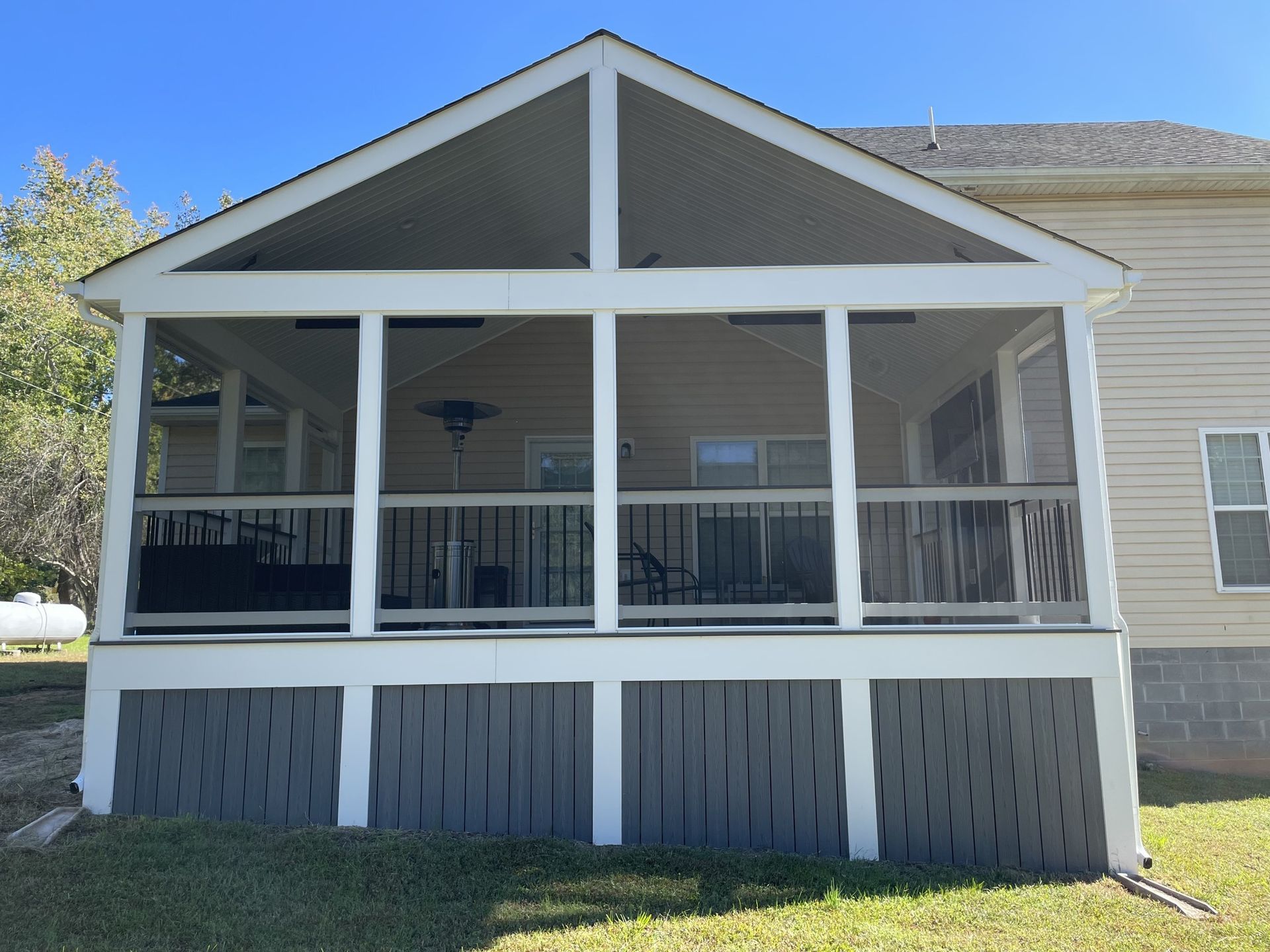 Front porch with white railing and gray gabled roof on a beige house, viewed from the yard