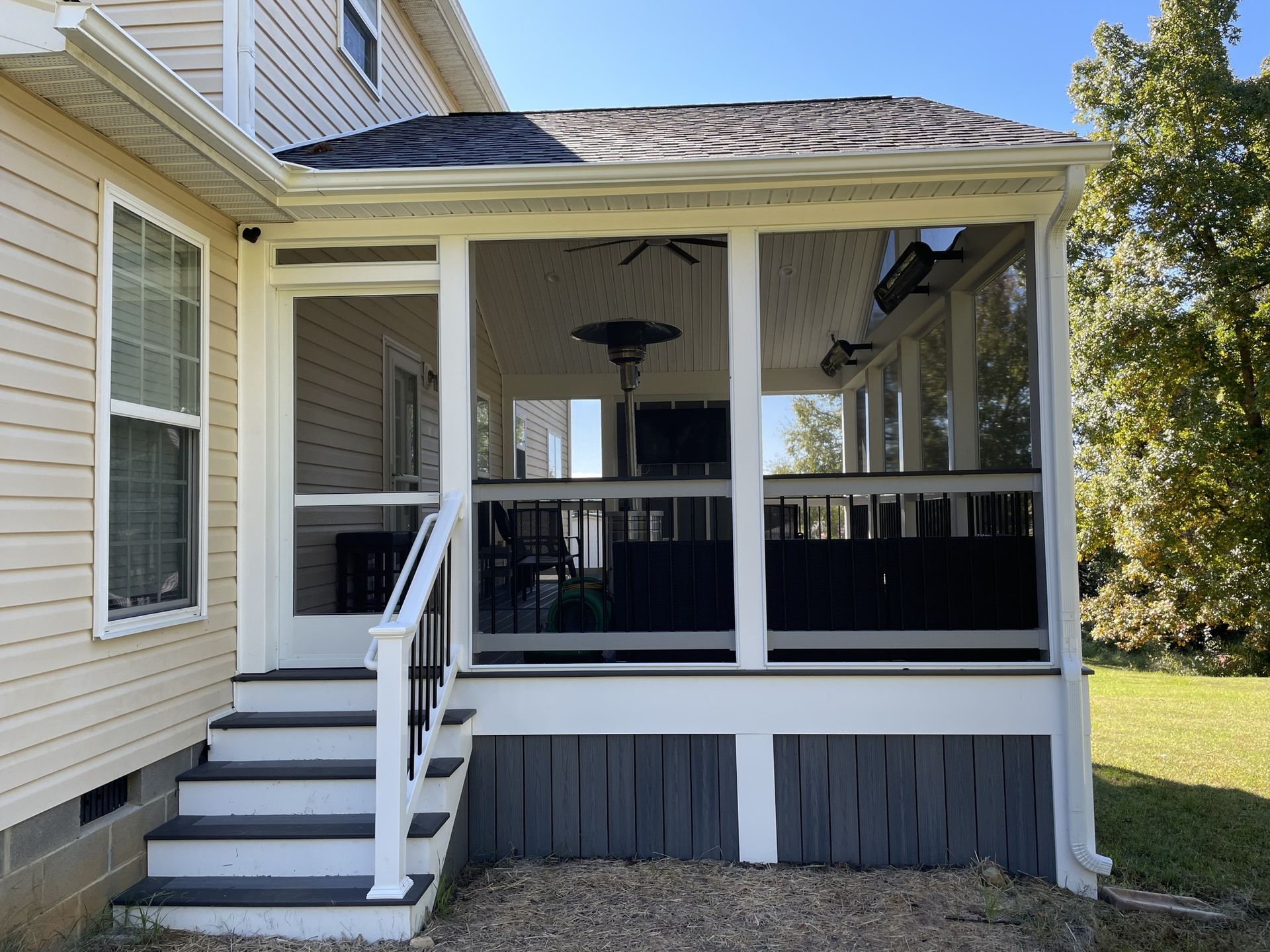 Covered backyard porch with white railings, black porch swing, and gray skirting on a beige house