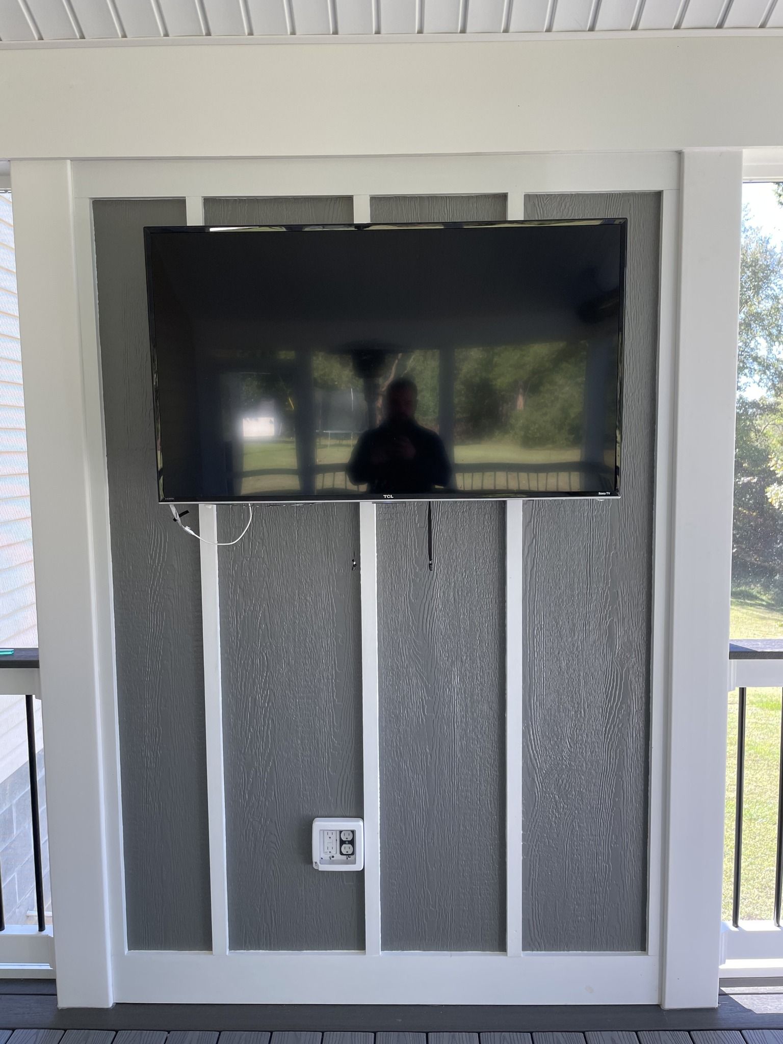 Wall-mounted TV above a gray decorative panel on a porch wall
