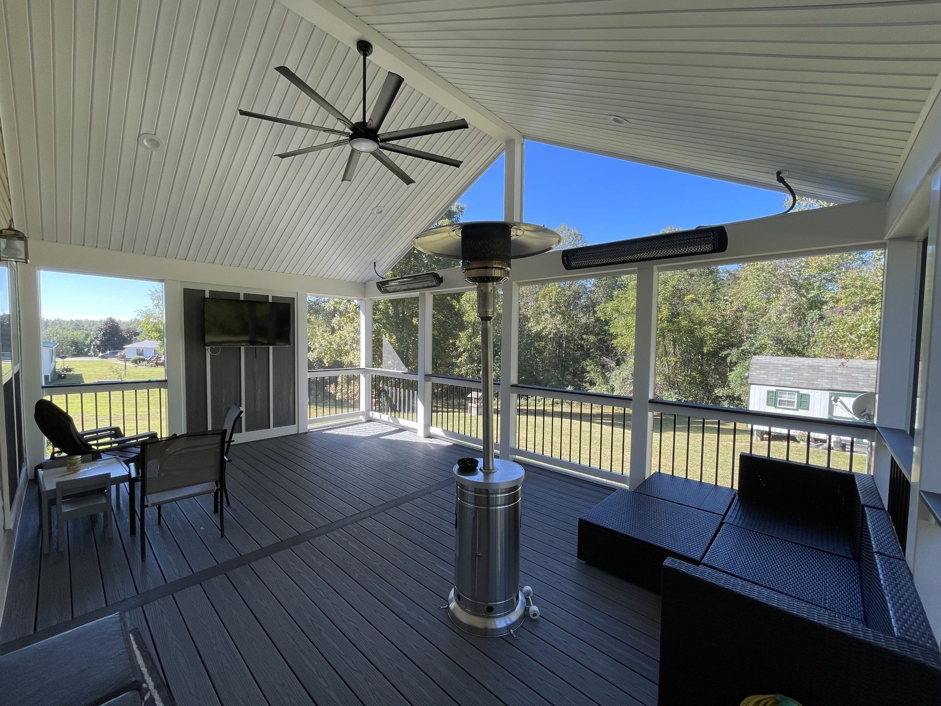 Covered patio with a ceiling fan, heater, seating, and open view of a golf course.