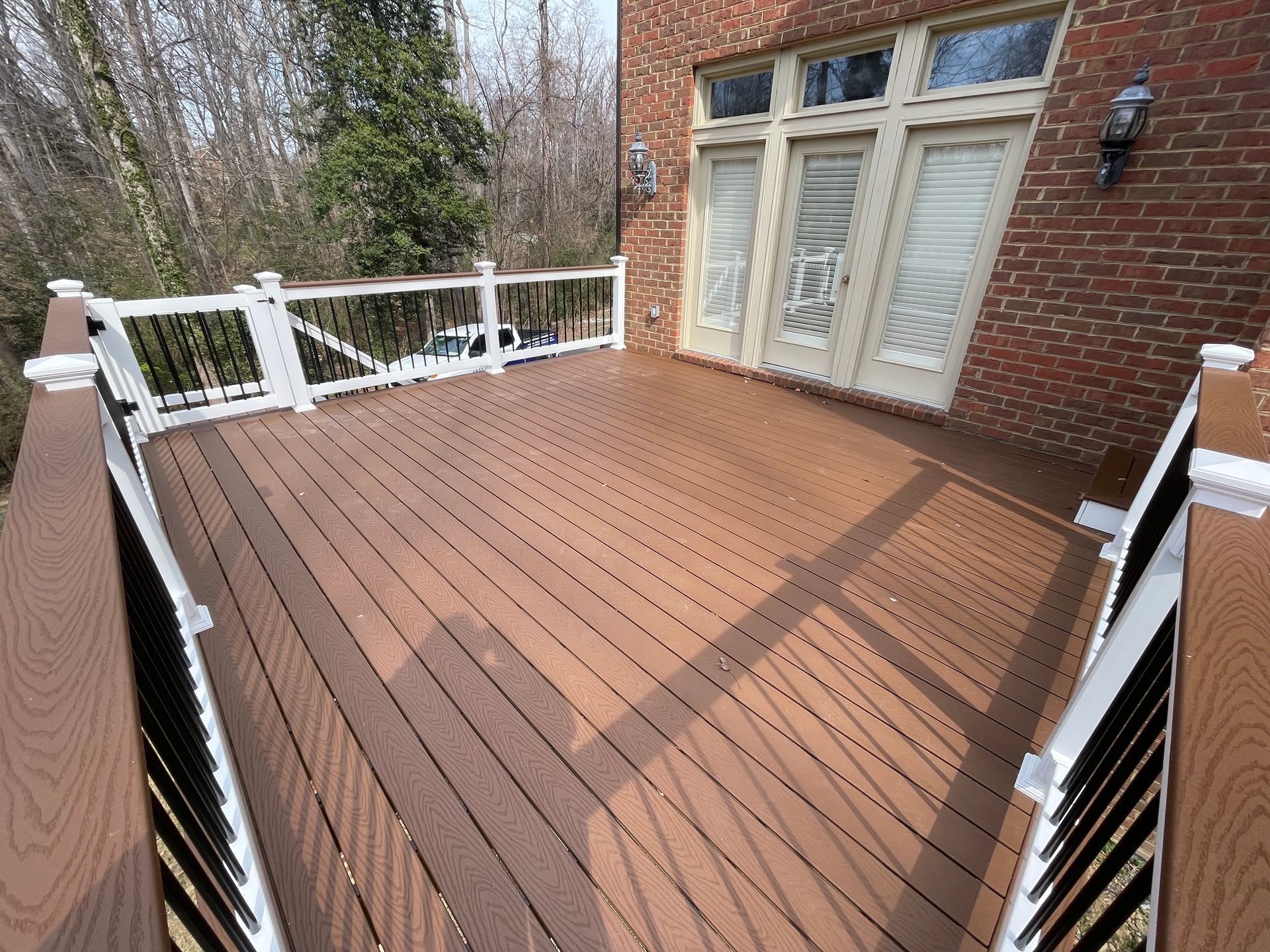 Wooden deck with white railings beside a brick house and French doors.