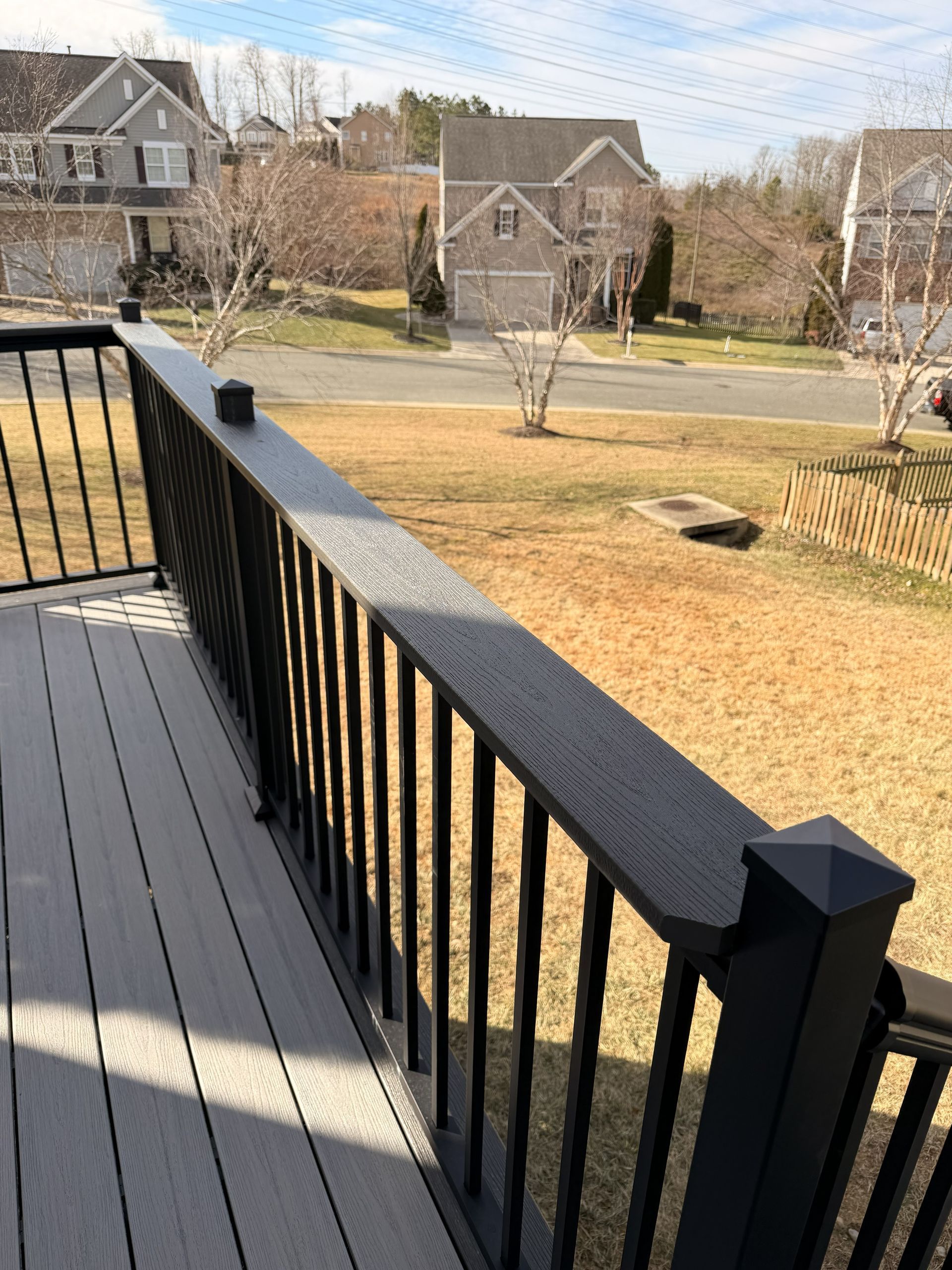 Front porch deck with black railing overlooking a suburban yard and neighboring houses.