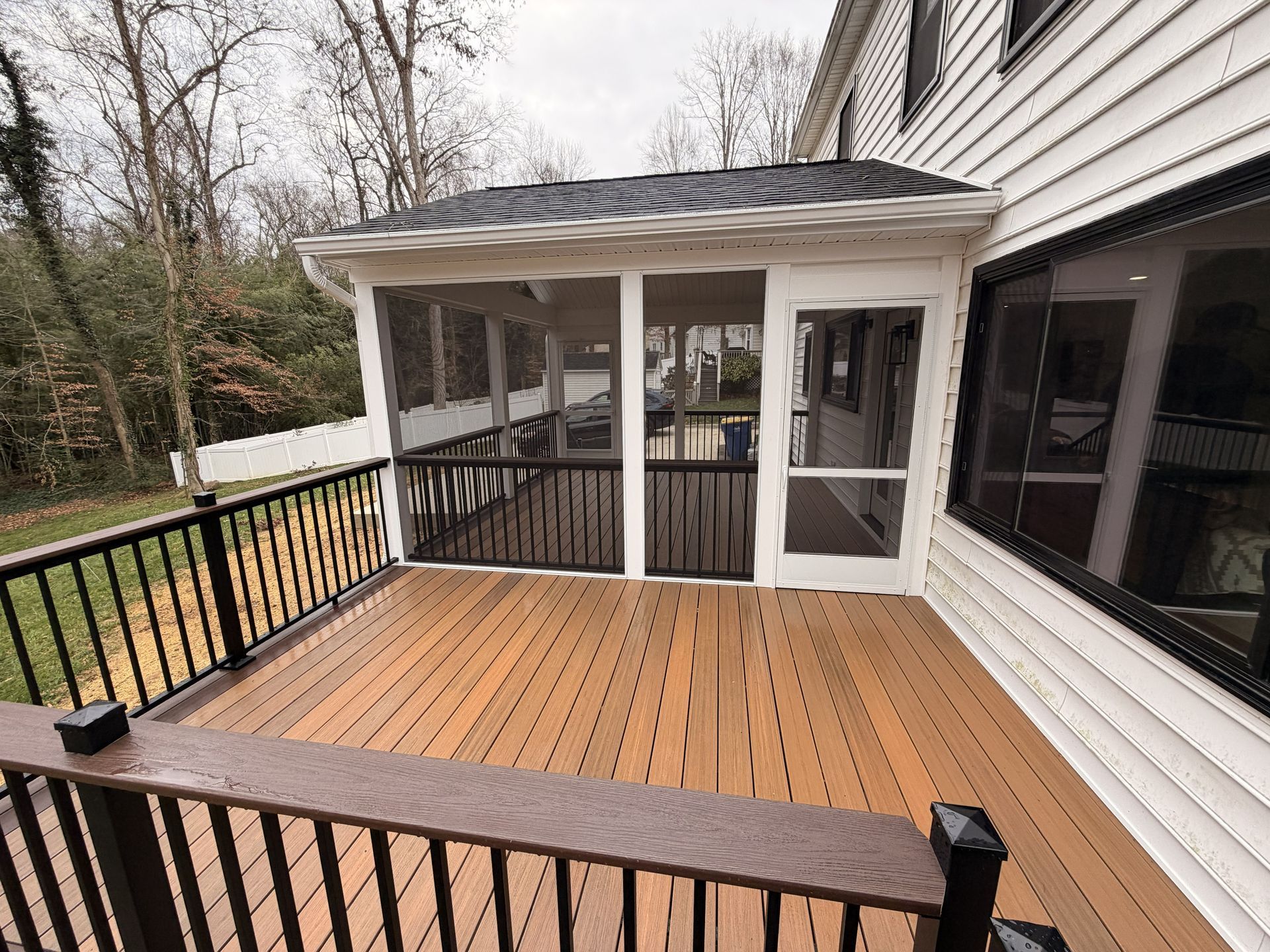 Wooden deck with black railing and screened gazebo beside a house, overlooking a yard.