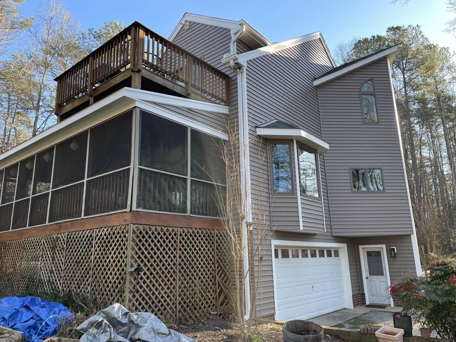 Gray house with screened porch, upper deck, and white garage under trees