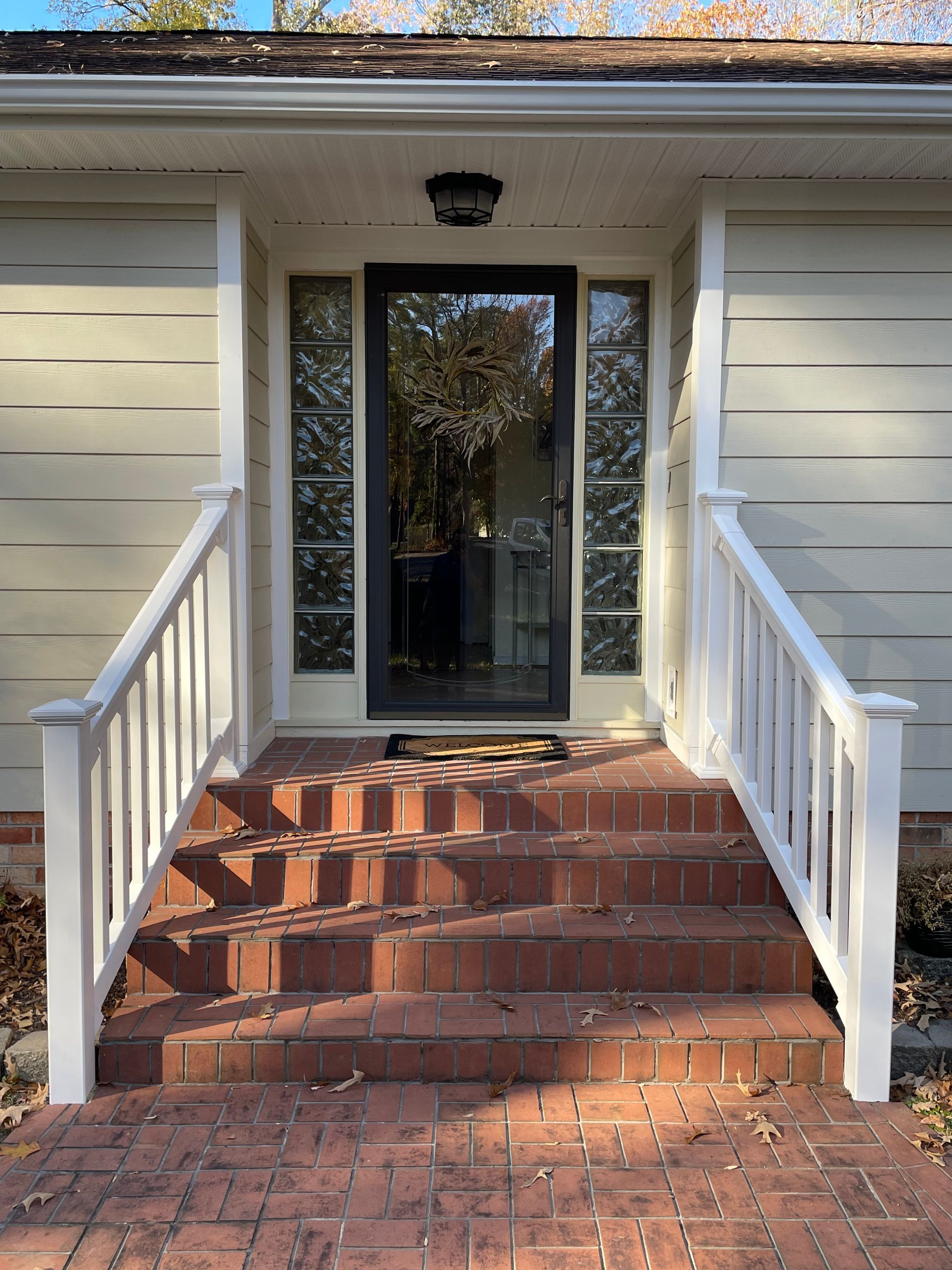 Front steps with red brick stairs and white railings leading to a glass front door.